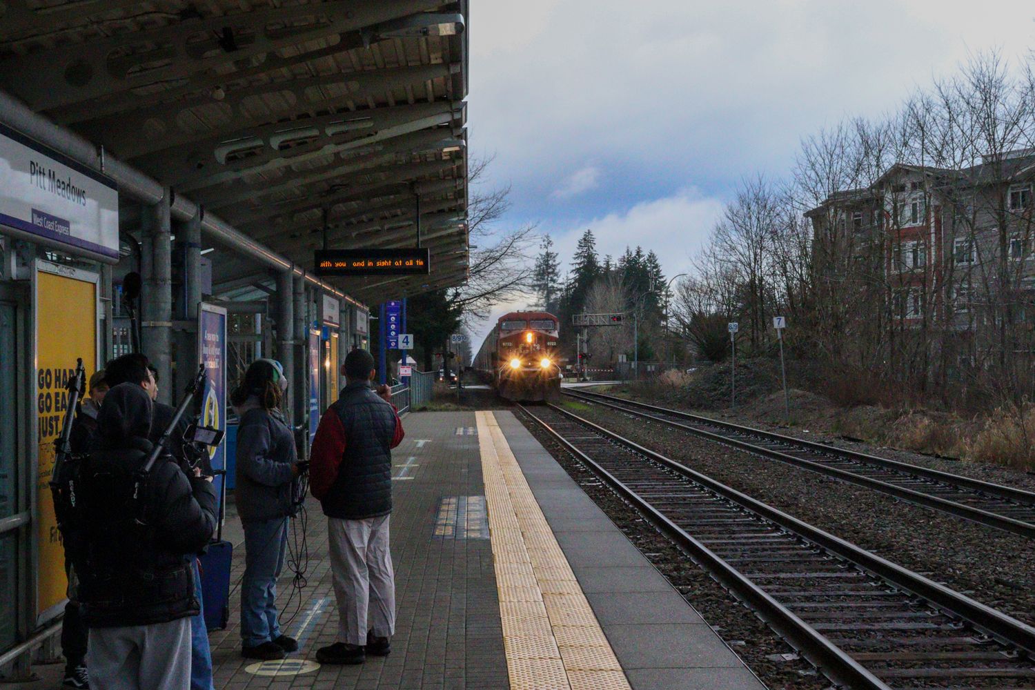 People waiting on a train platform as a commuter train approaches at dusk.
