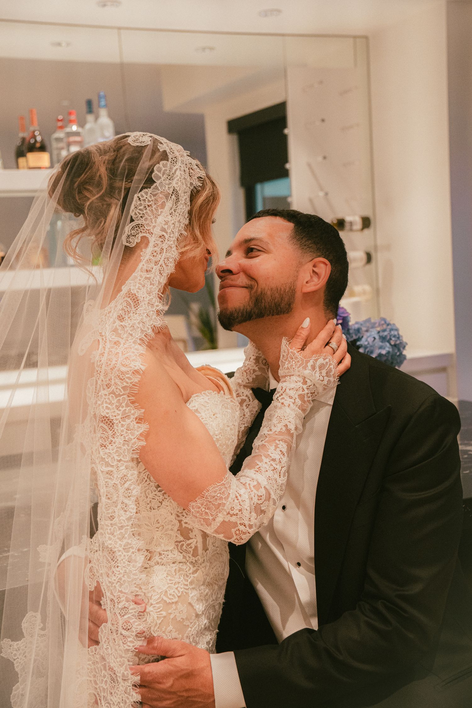 Bride in lace gown and veil shares romantic moment with groom in black tuxedo at wedding reception.