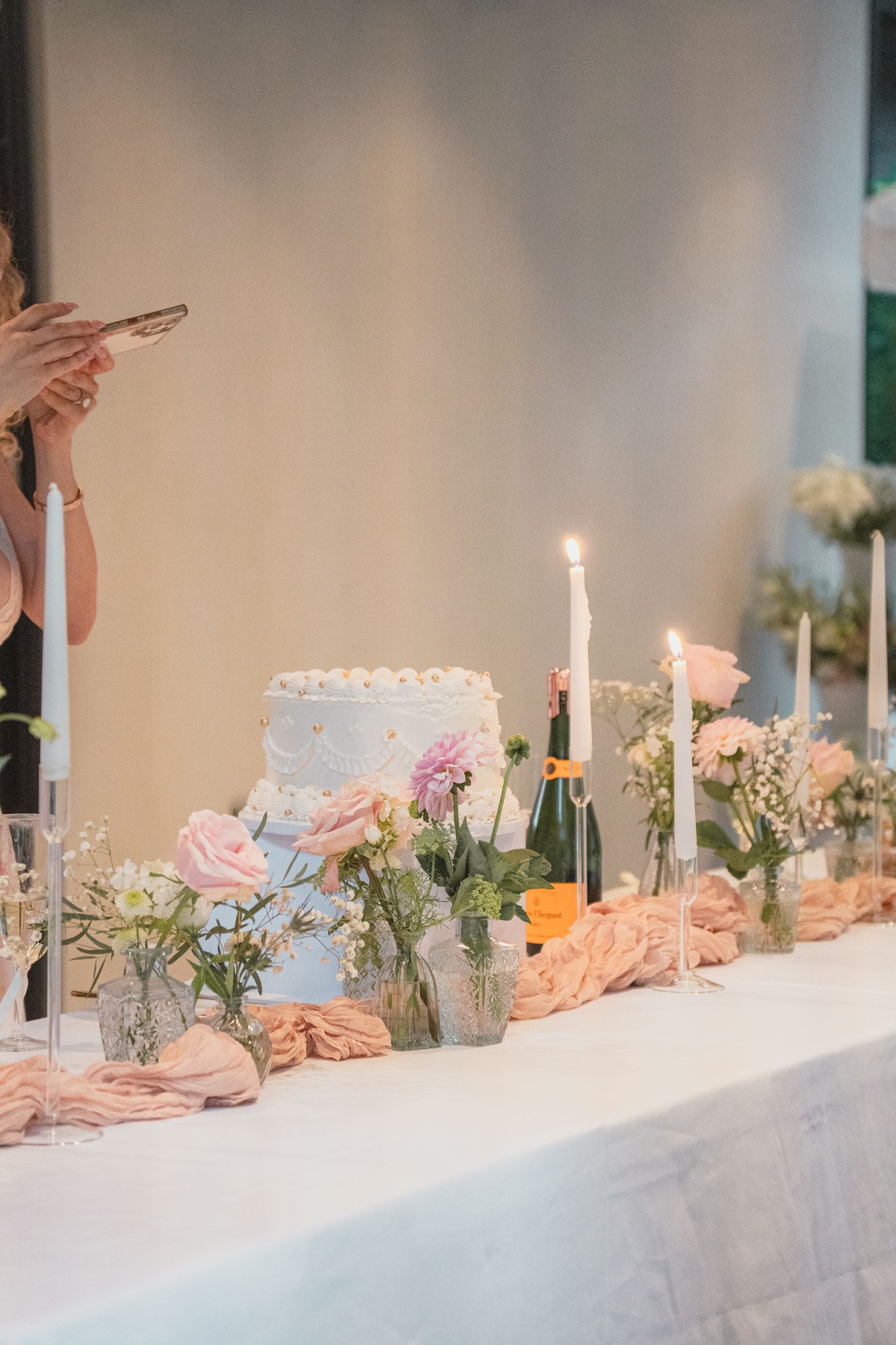 Elegant wedding reception table with tiered cake, candles, champagne and pink floral arrangements.