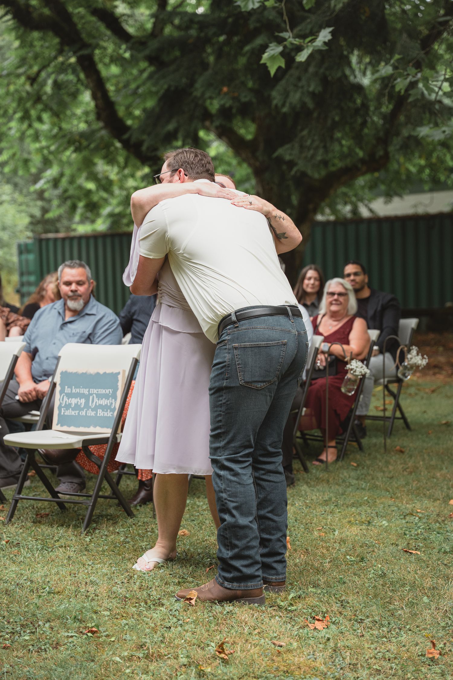 A man and woman share an emotional hug during an outdoor wedding ceremony on a green lawn.