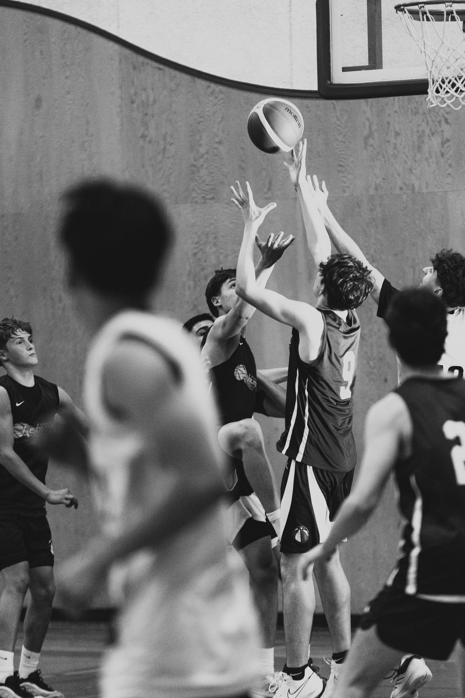 Black and white photo of young basketball players competing for the ball during an indoor game.
