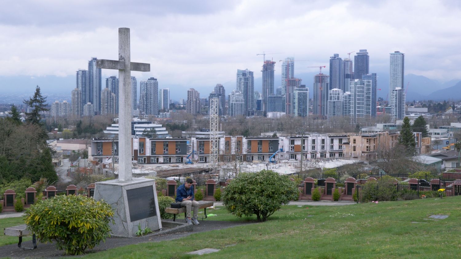 Large stone cross monument overlooking a urban skyline with modern high-rise buildings in Vancouver.