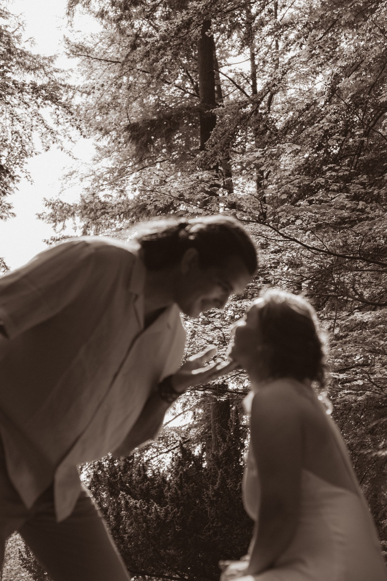 Sepia-toned wedding photo of bride and groom sharing romantic moment in forest setting.