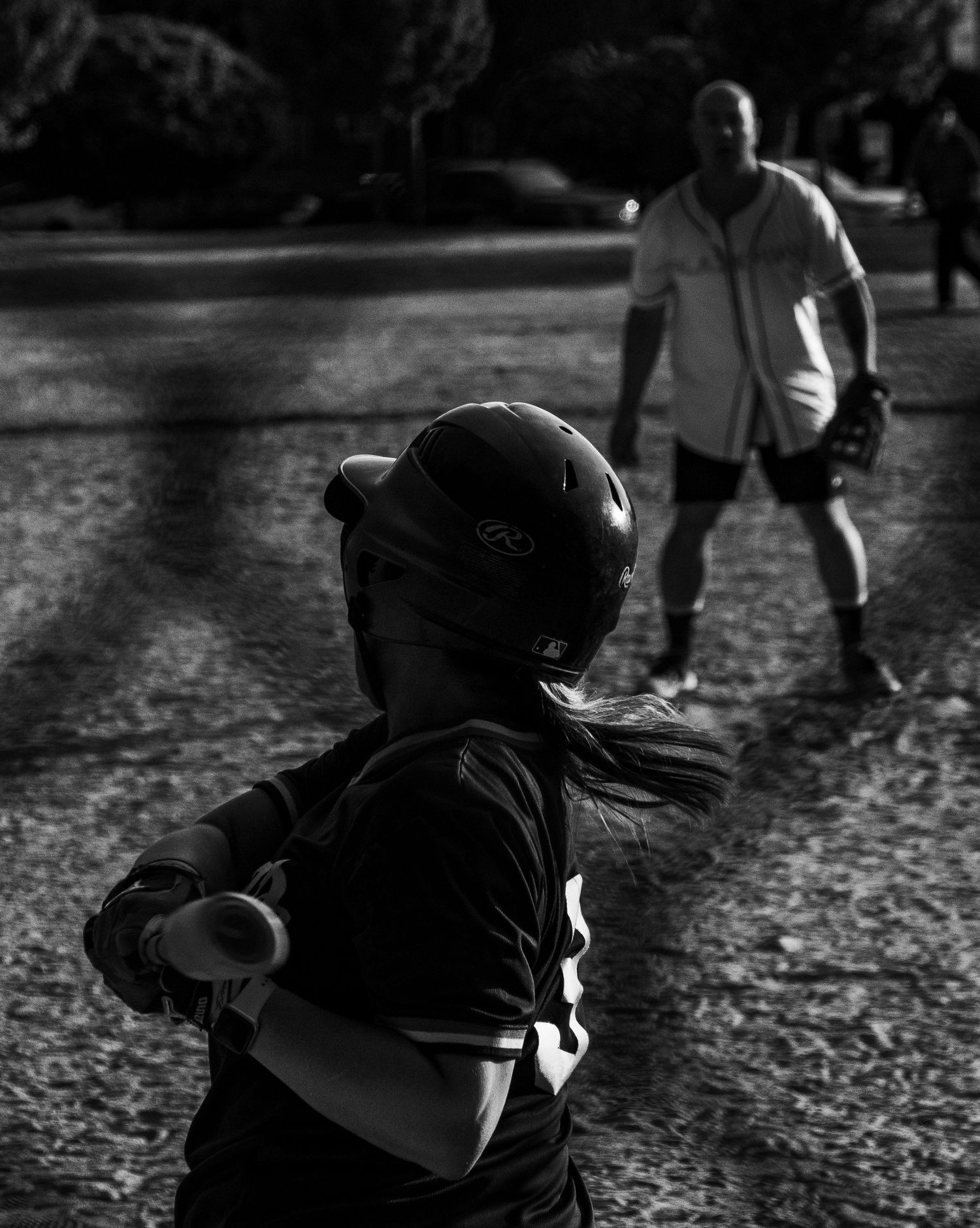 Black and white photo of a young softball batter facing a fielder on a dirt playing field.