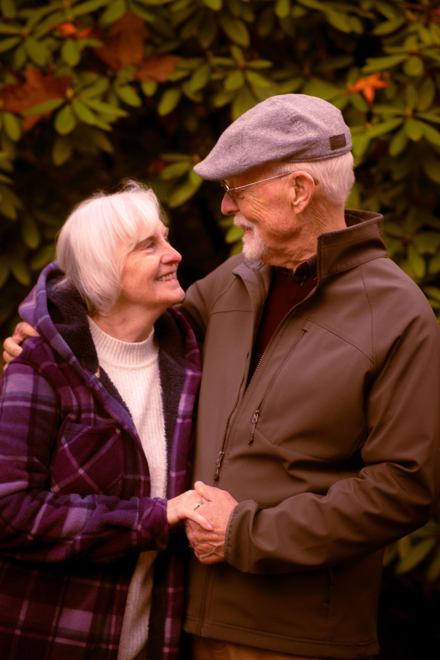 Happy senior couple holding hands and smiling at each other with colorful autumn foliage in background.