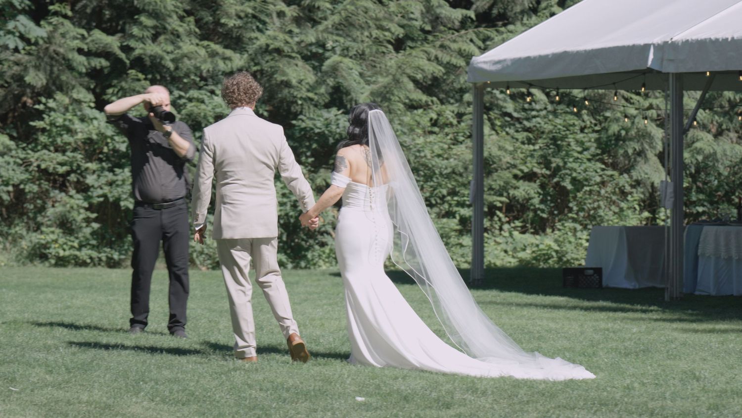 Newlywed couple walks hand in hand across green lawn after outdoor wedding ceremony.
