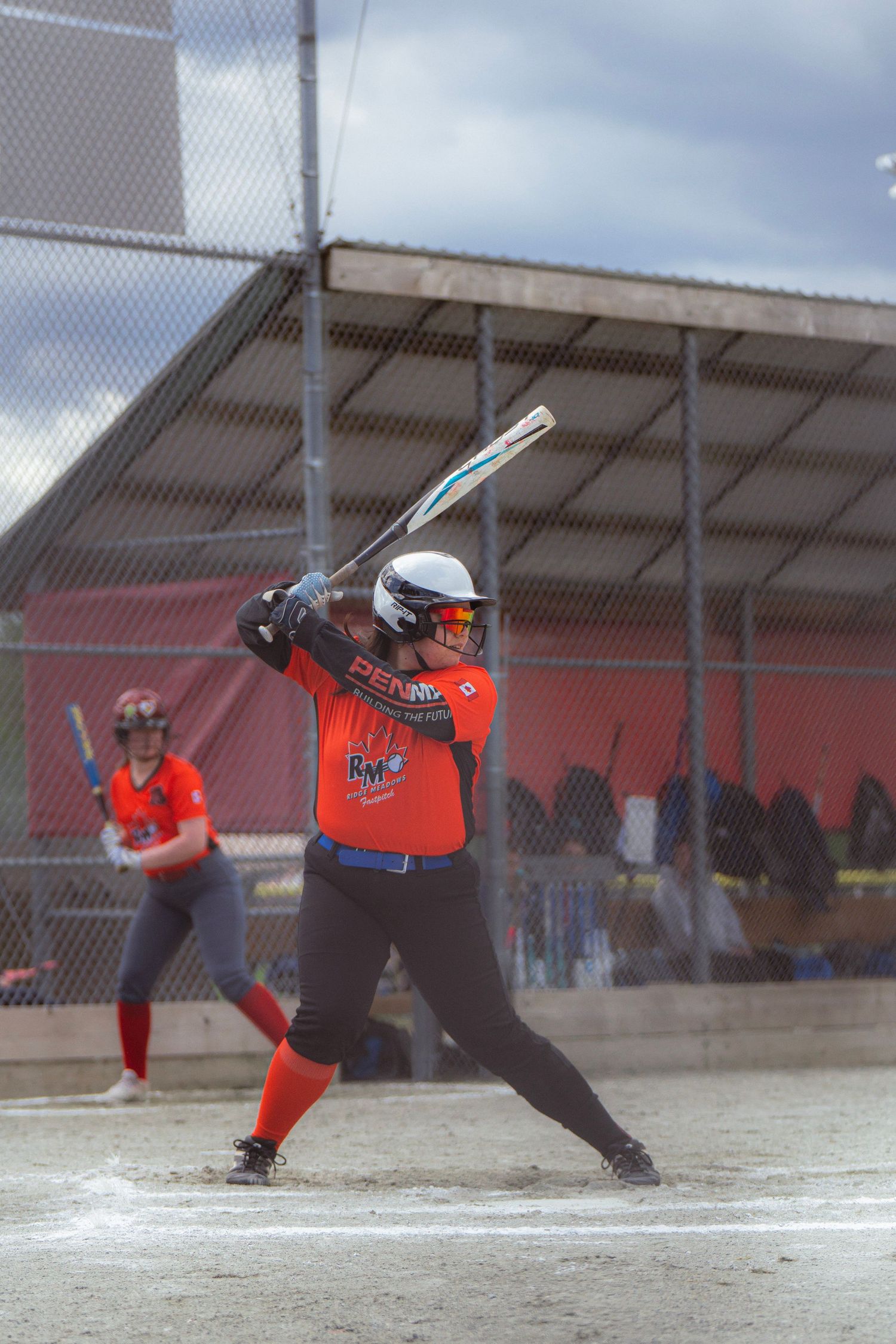 Female softball player in orange uniform at bat, ready to swing at home plate during a game.