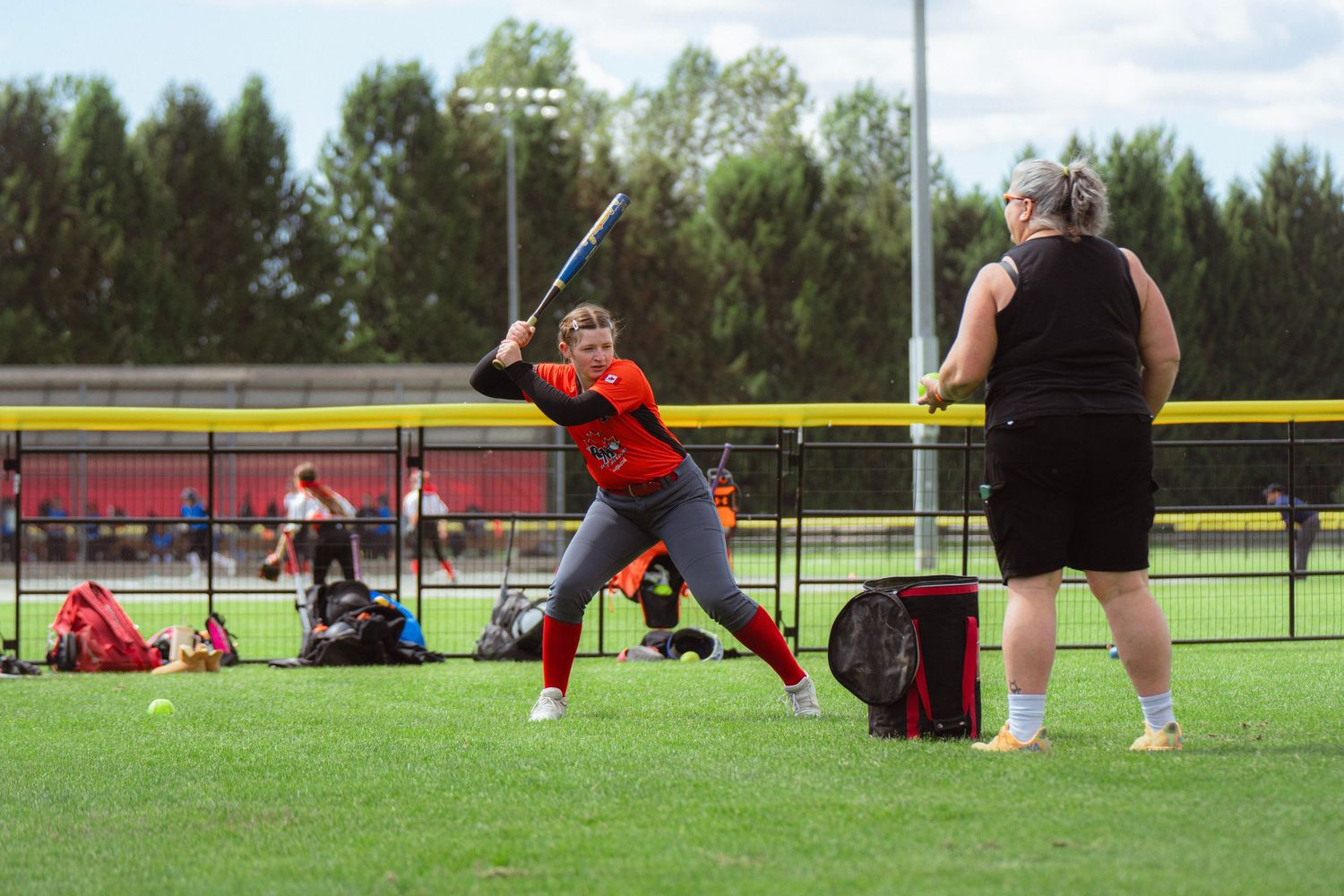 Female softball player in orange uniform taking a swing during outdoor batting practice session.