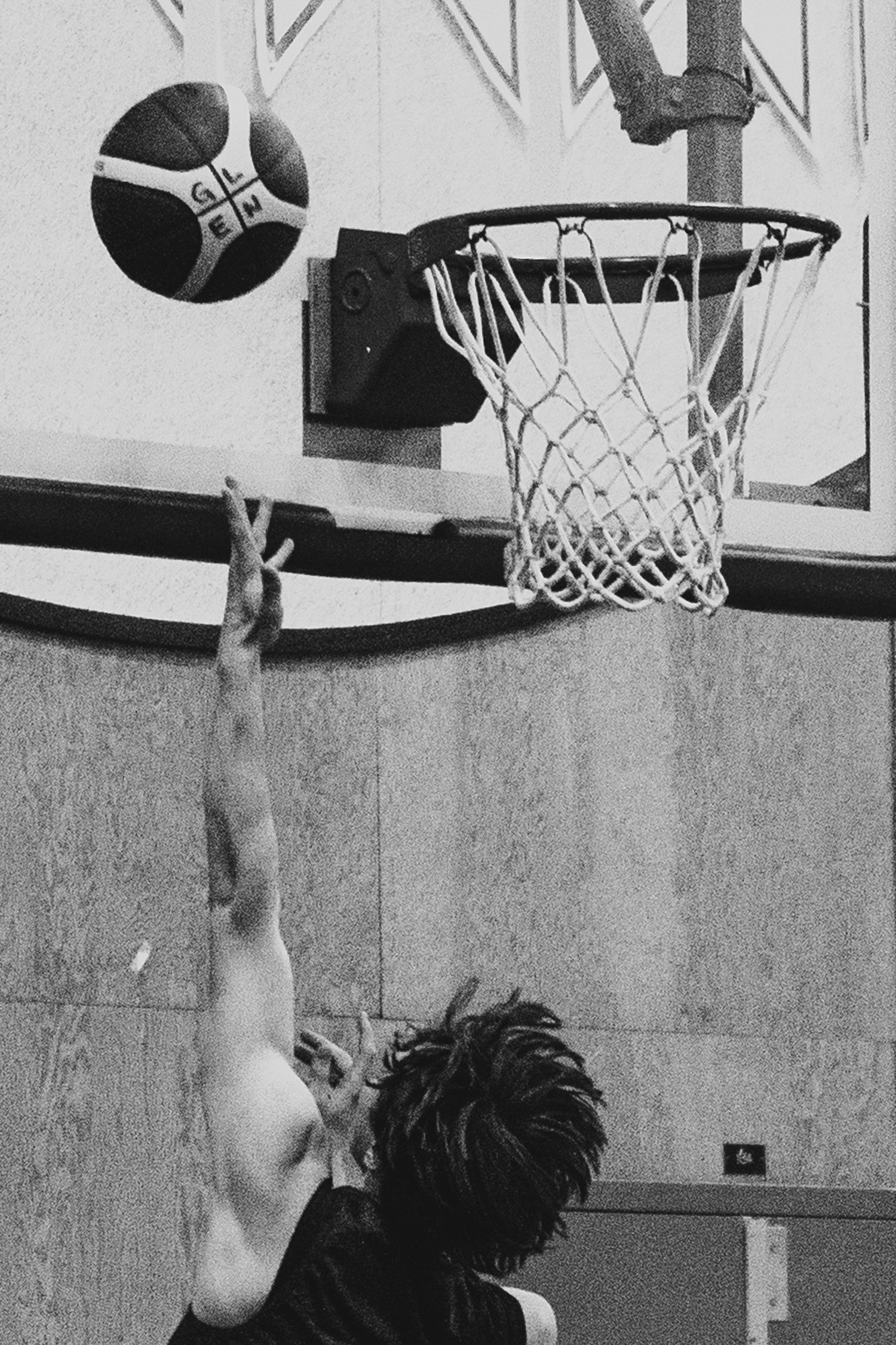 Basketball player reaches up to shoot layup toward hoop in black and white photo.