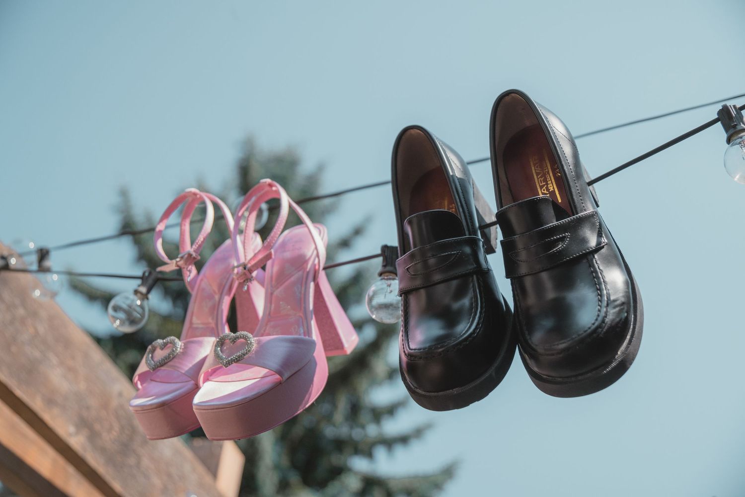 Pink high-heel sandals and black loafers hanging on a wire against a blue sky backdrop.