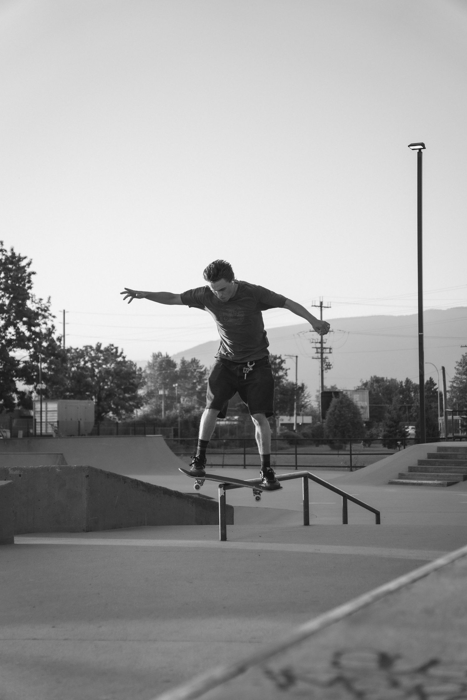 Black and white photo of a skateboarder grinding a rail at an outdoor skate park.