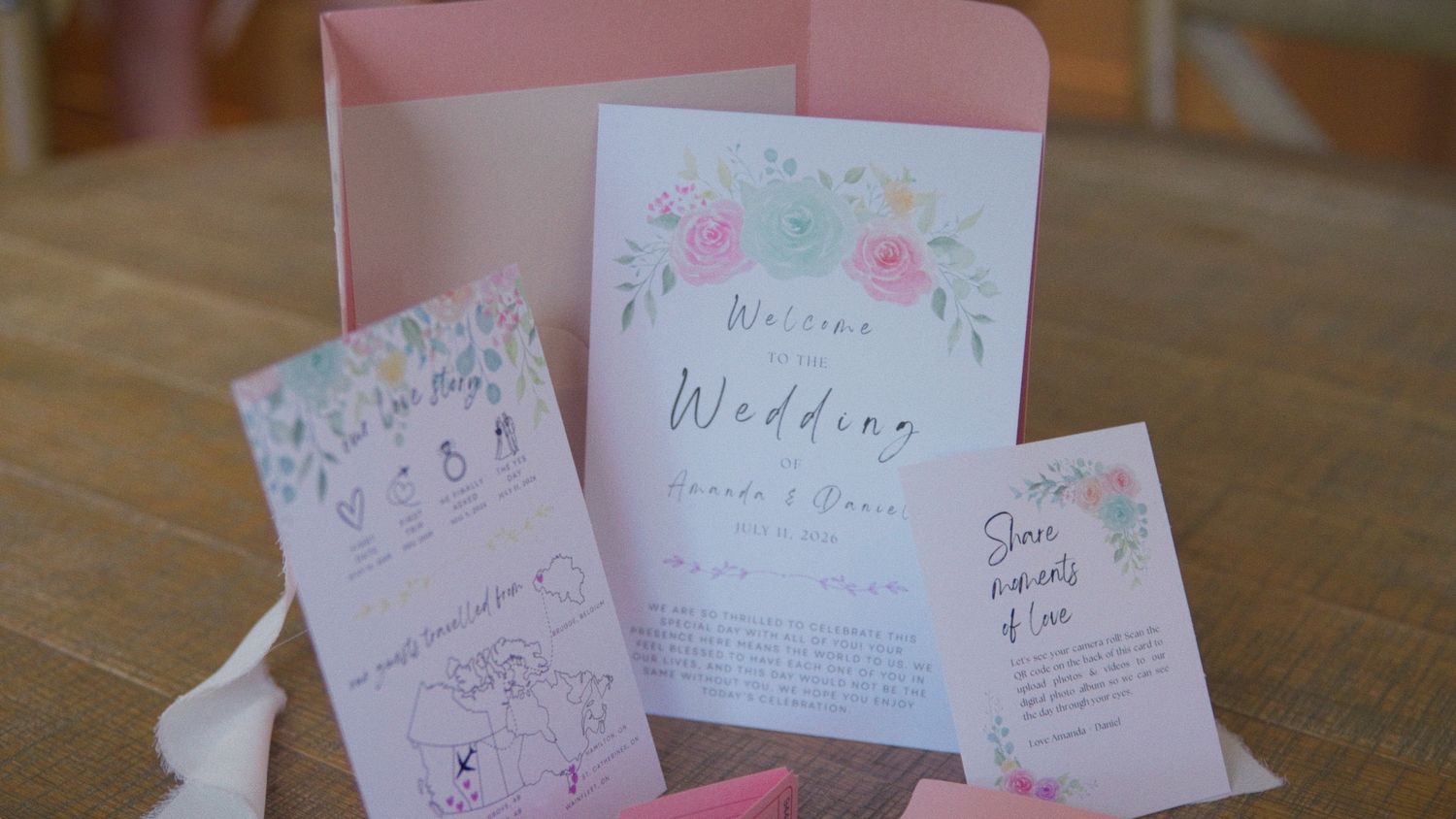 Elegant floral wedding stationery set with pink watercolor flowers, including invitation, program, and menu cards on a wooden table.