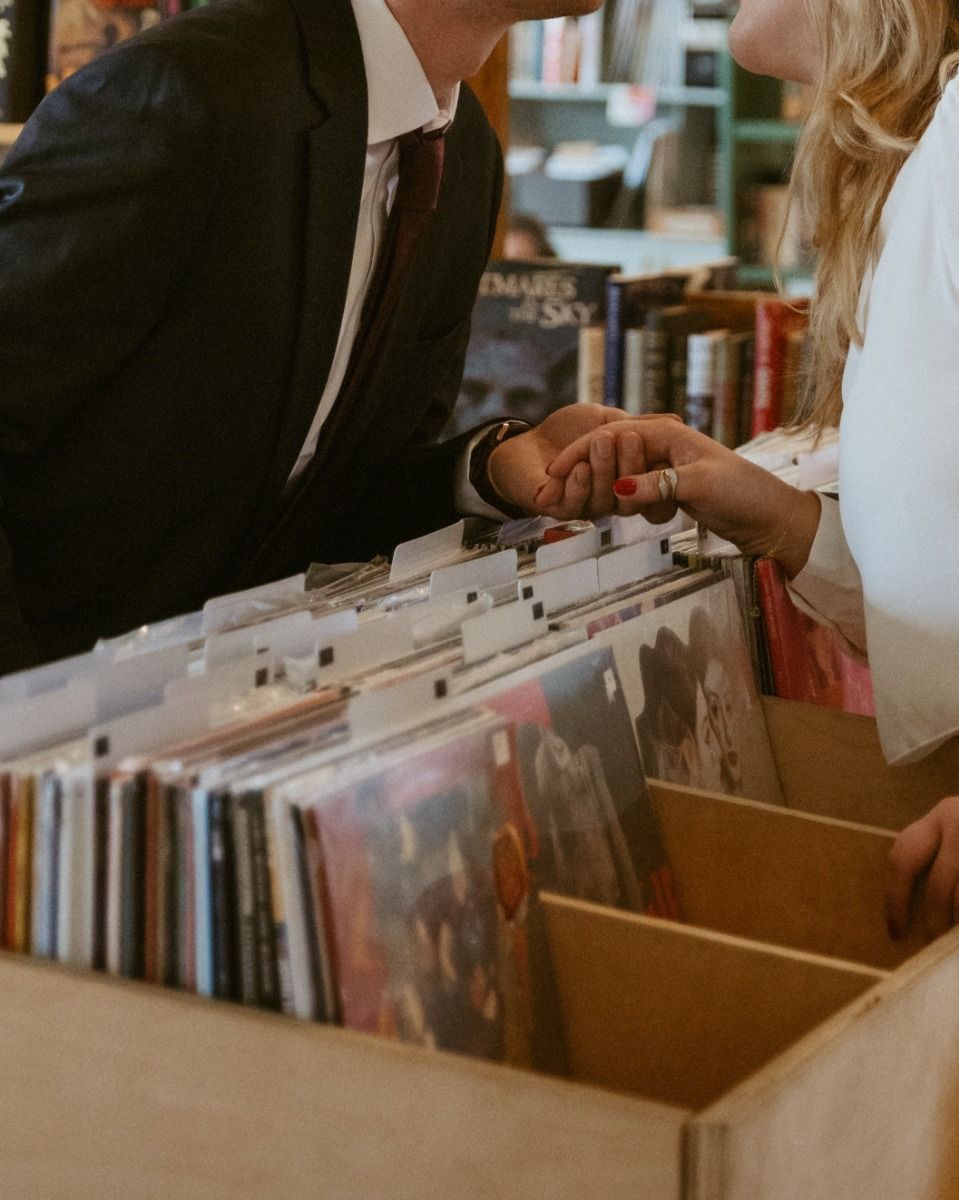 Couple browsing vinyl records in a music store, holding hands over a box of albums.
