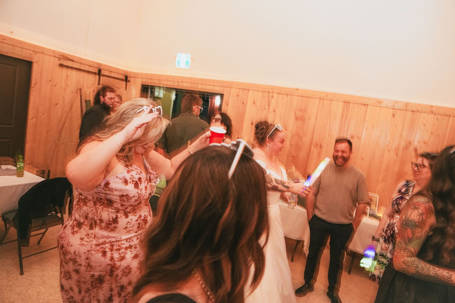 Guests dancing and celebrating at a wedding reception in a rustic wooden venue with warm lighting.