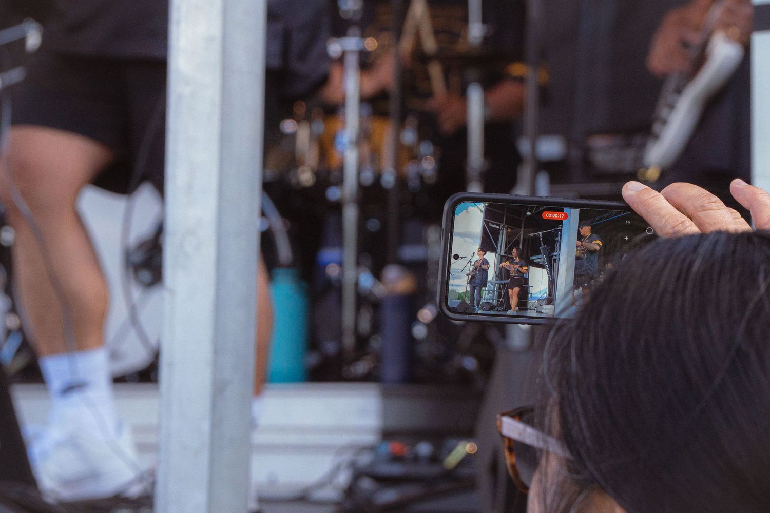 Audience member records a live outdoor concert performance on a smartphone at a music festival.