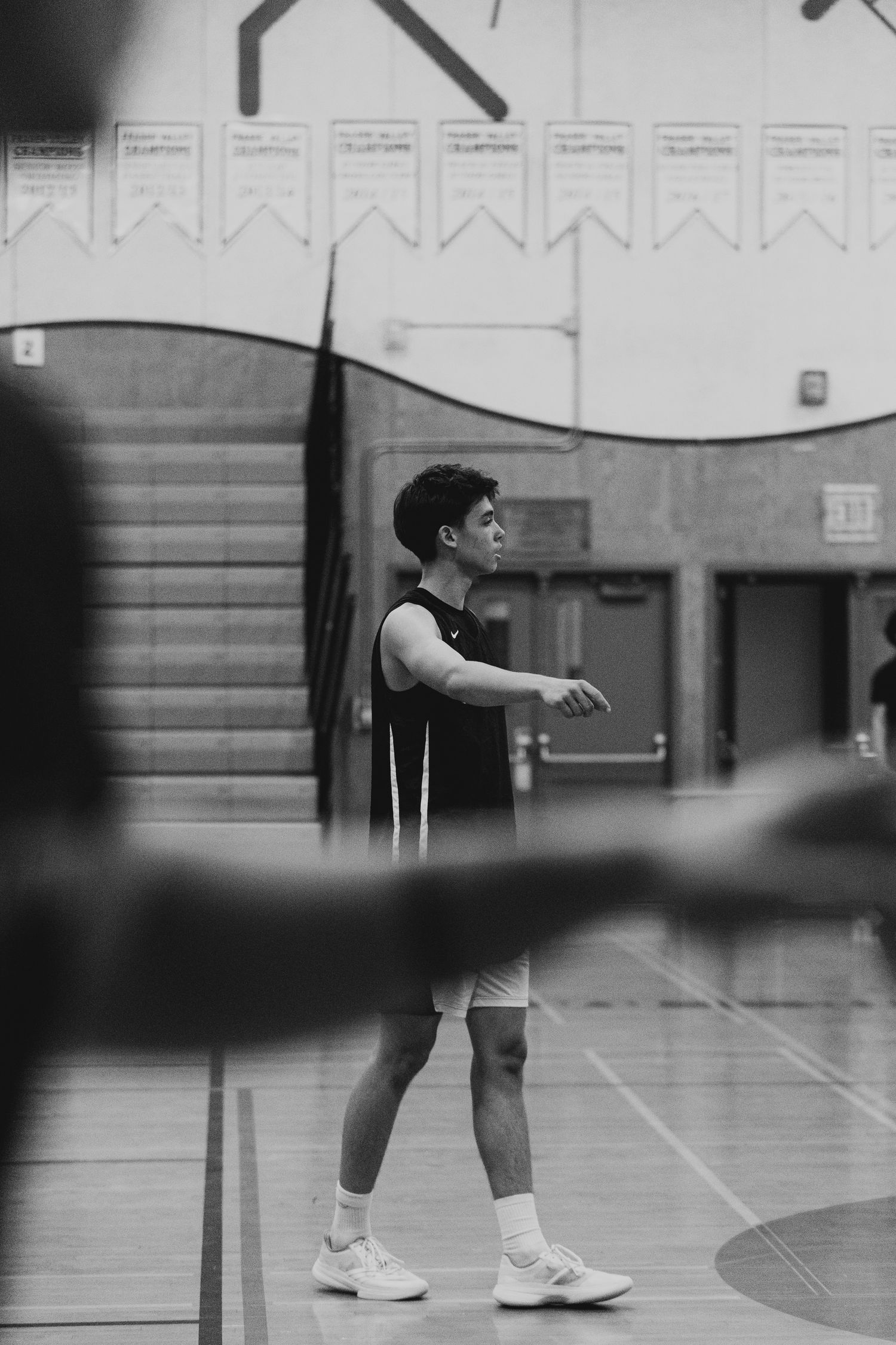Black and white portrait of a young male basketball player standing on an indoor court in athletic uniform.