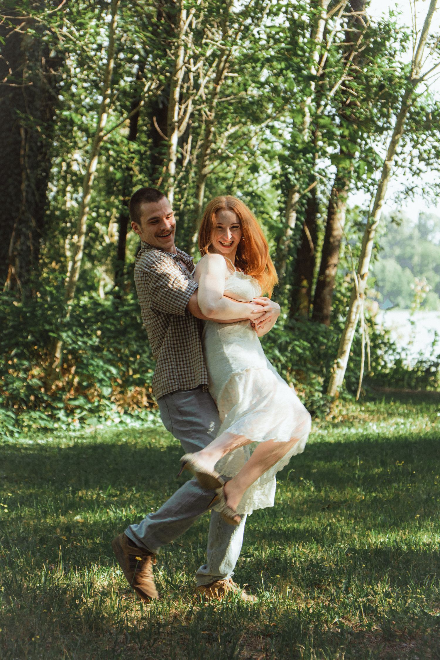 A joyful couple dancing and embracing in a lush green park, woman in white dress with flowing red hair.
