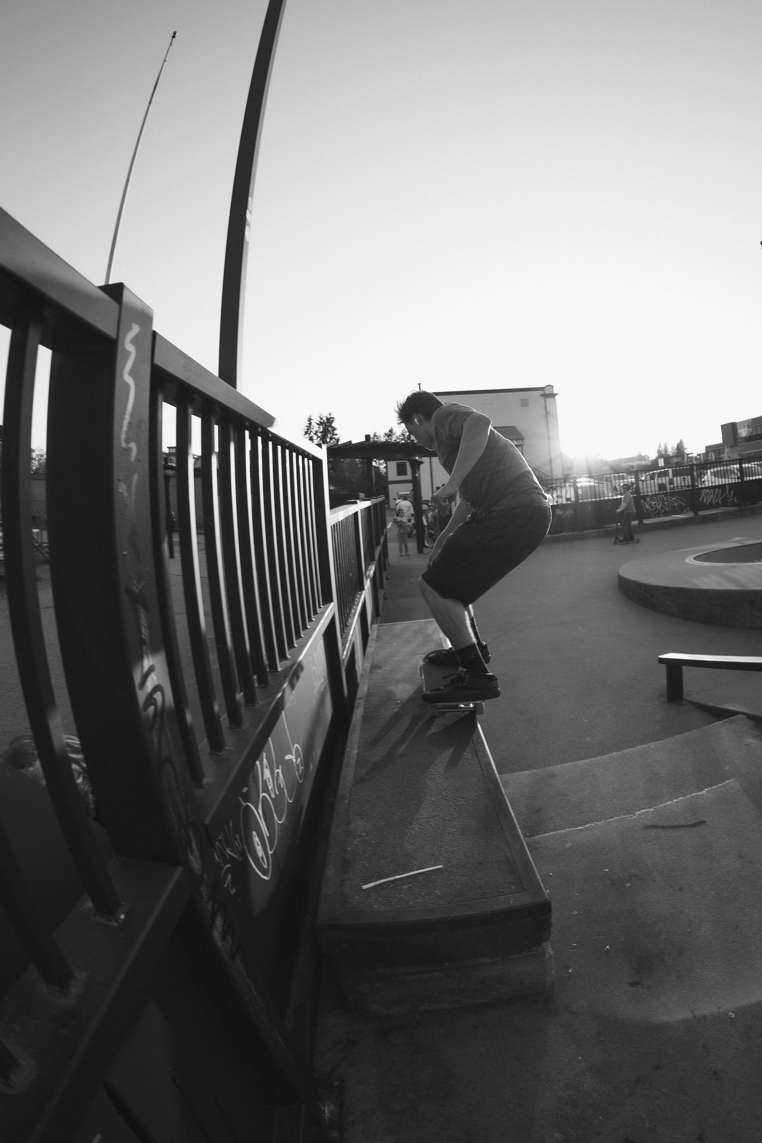 Black and white image of skateboarder grinding a concrete ledge at a skate park at dusk.