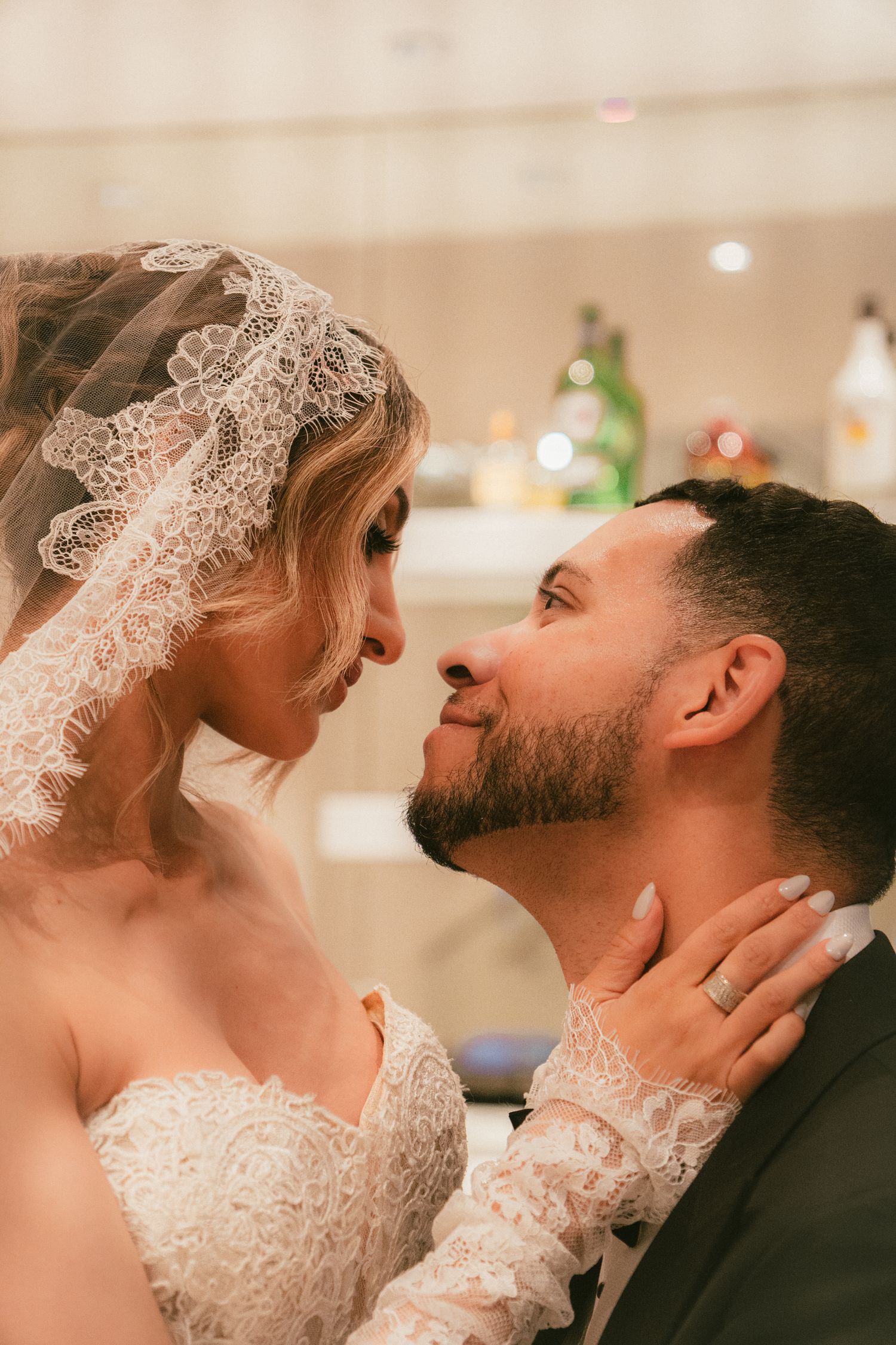 Bride in lace veil and groom sharing a romantic moment, faces close together during wedding celebration.