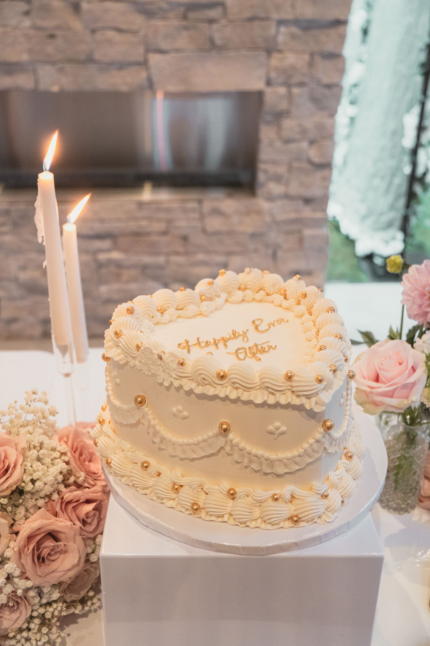 Heart-shaped two-tier wedding cake with gold pearl details and Happily Ever After inscription.