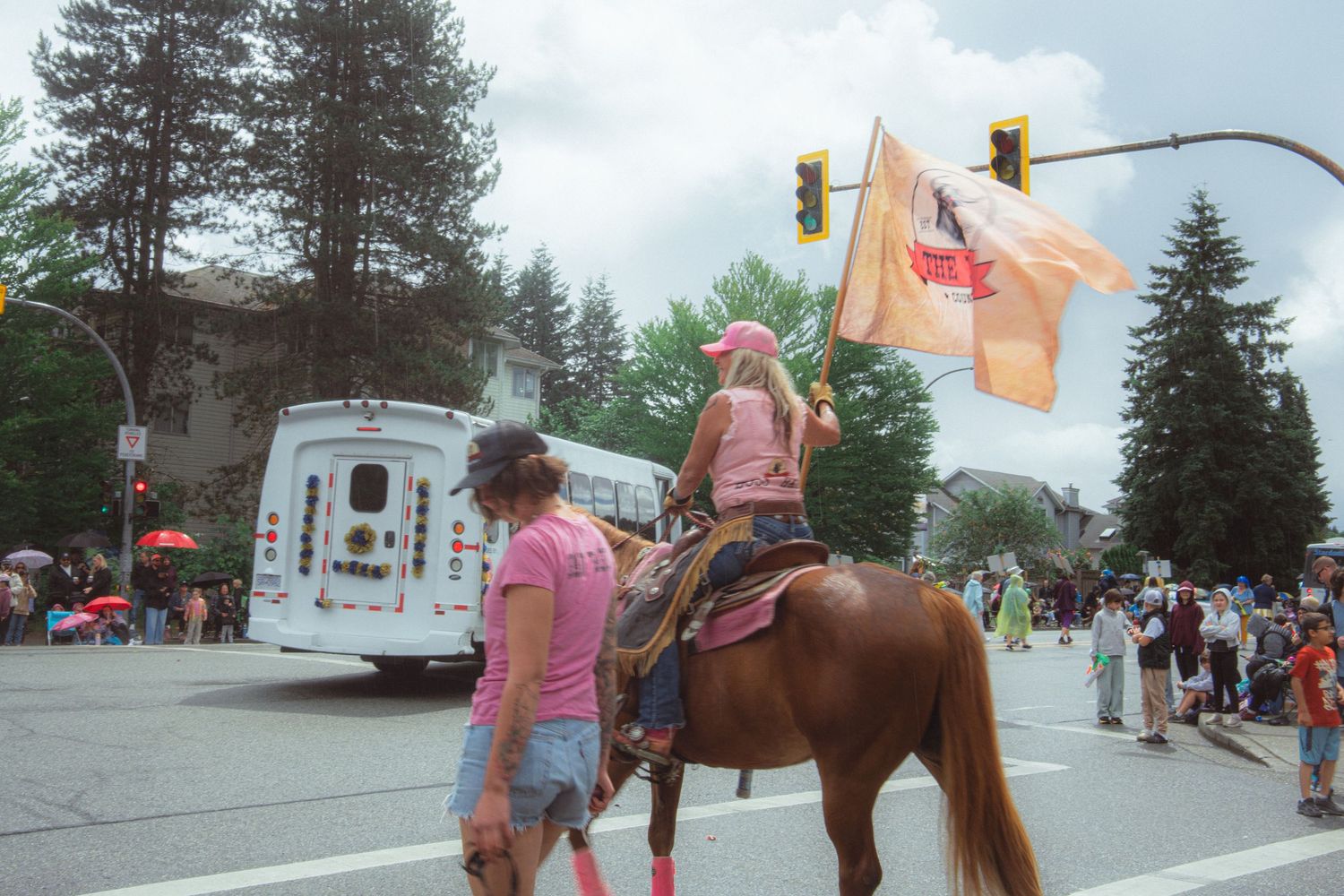 A young girl on horseback carries a flag during a colorful outdoor parade on a busy street.