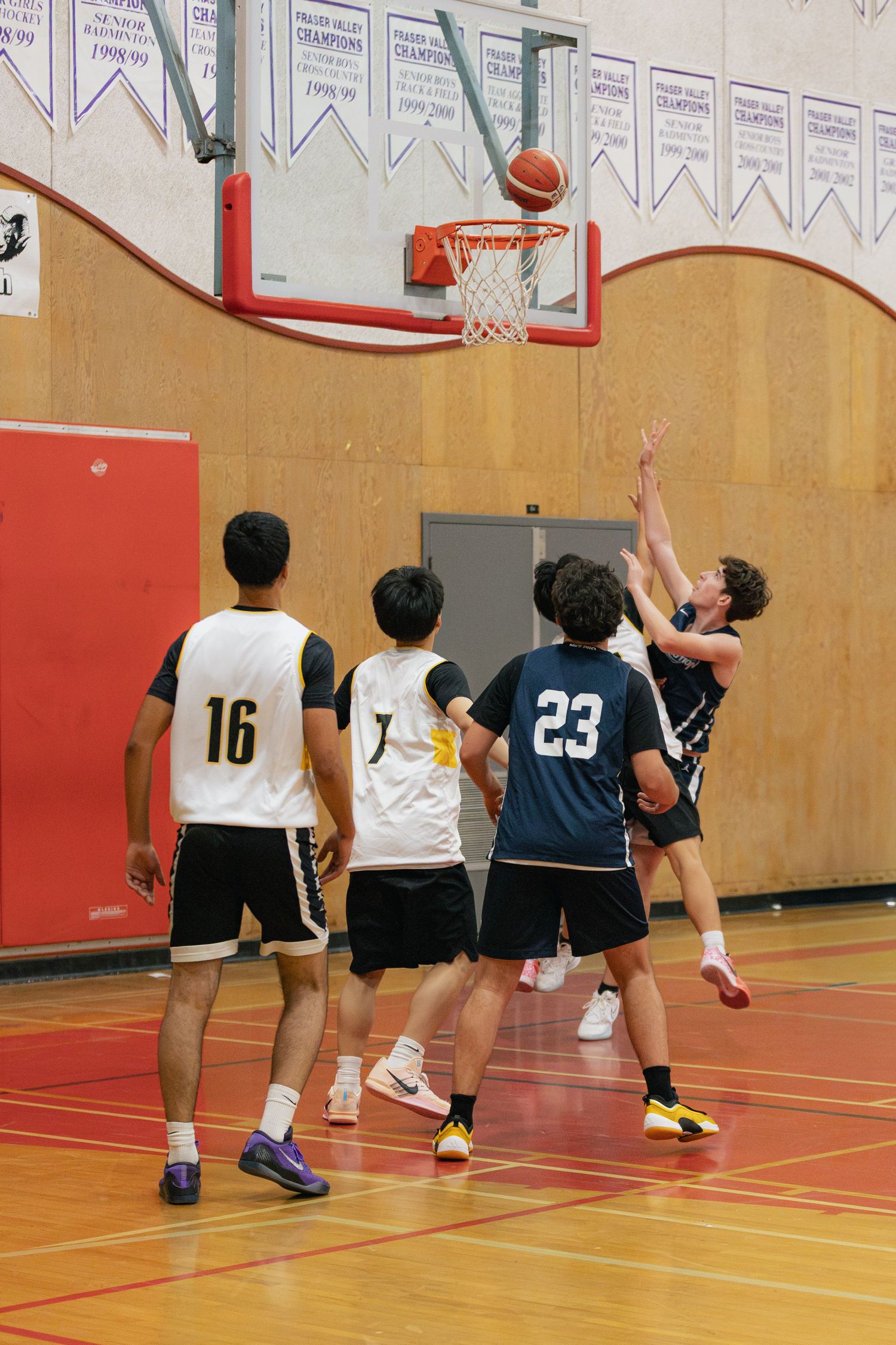 Basketball players battle under the hoop during an indoor game with spectators watching.