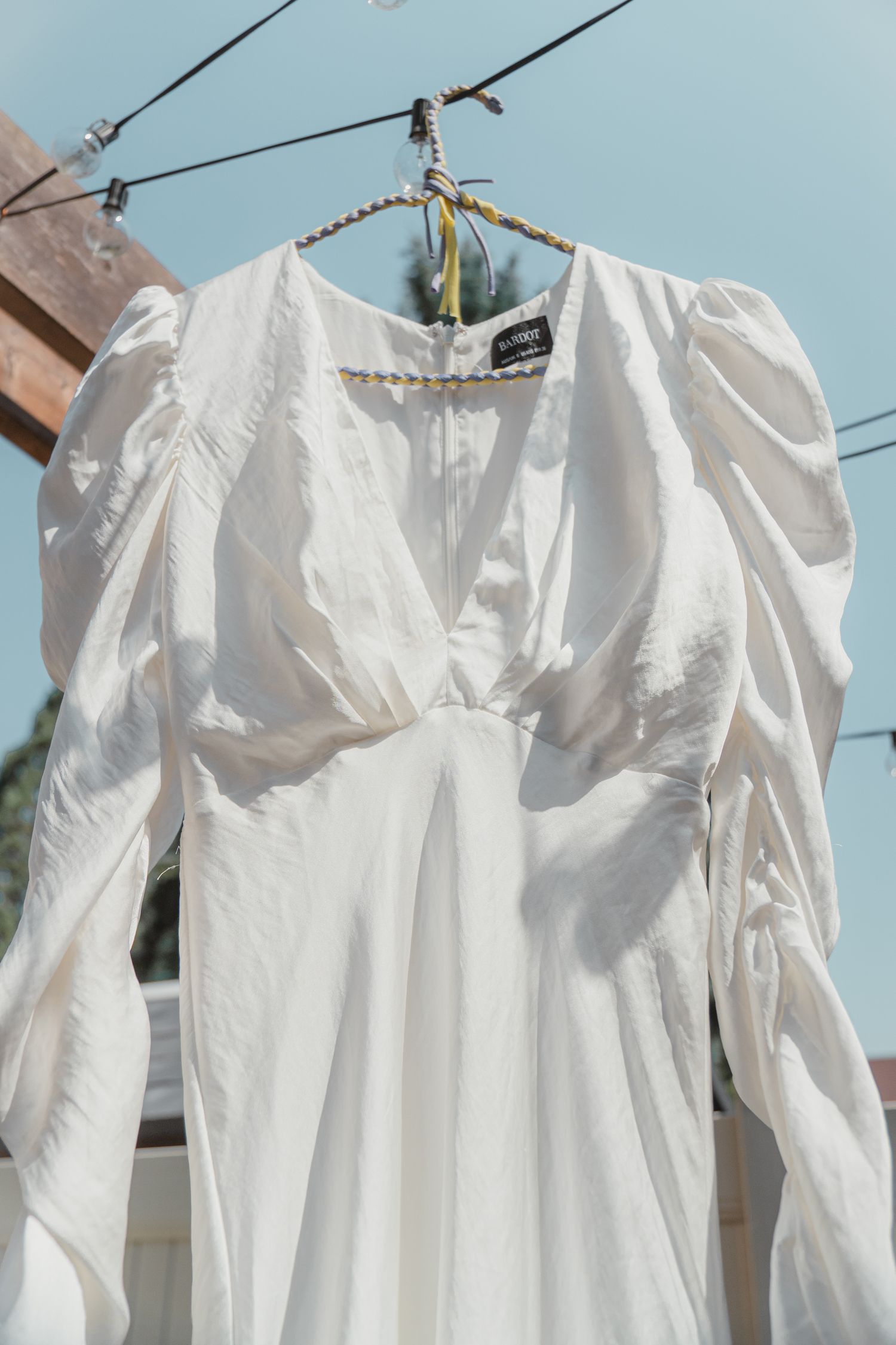White wedding dress with puff sleeves hanging on a hanger outdoors against a blue sky.