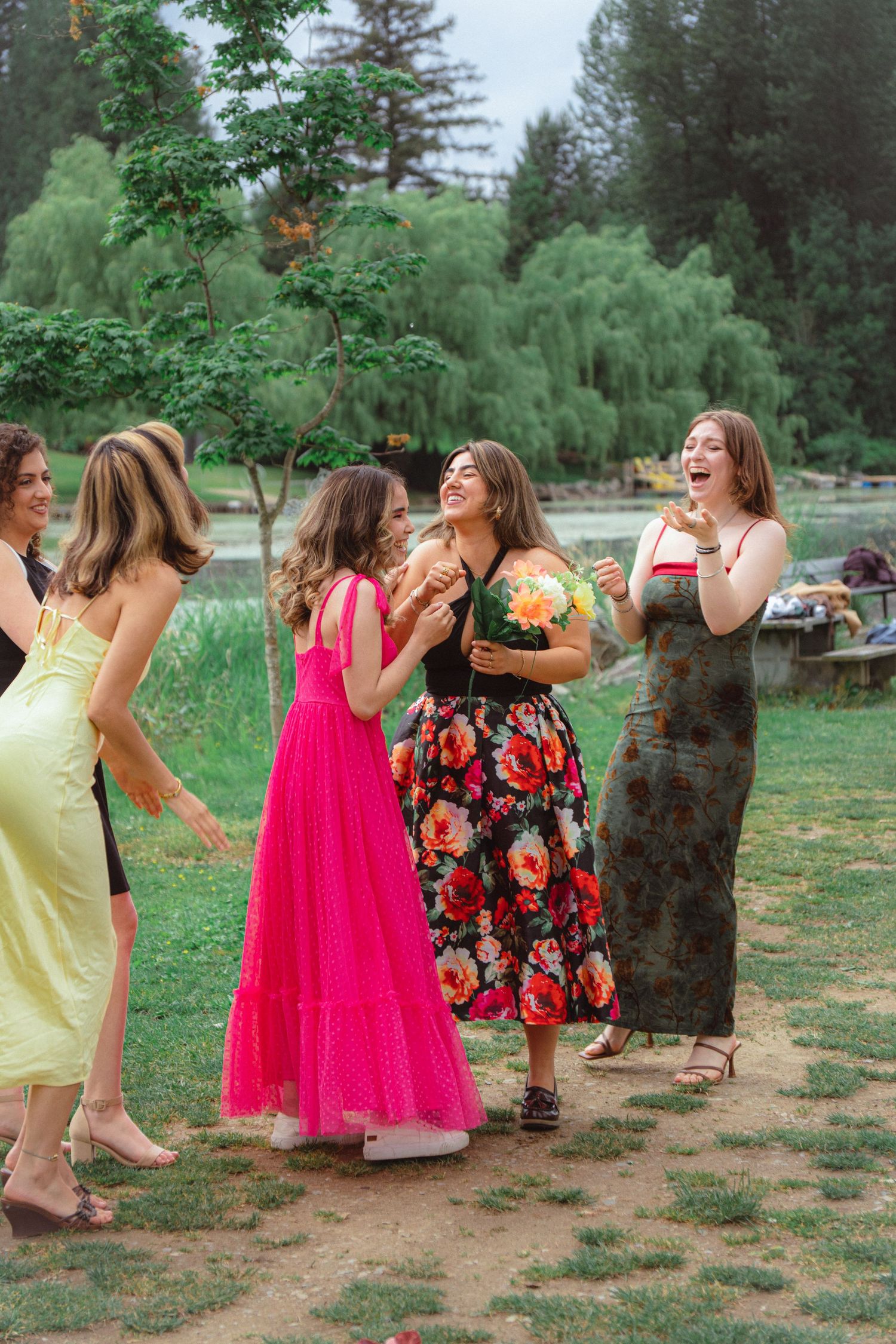 Bridesmaids in colorful dresses laughing and celebrating after catching bouquet at outdoor wedding.
