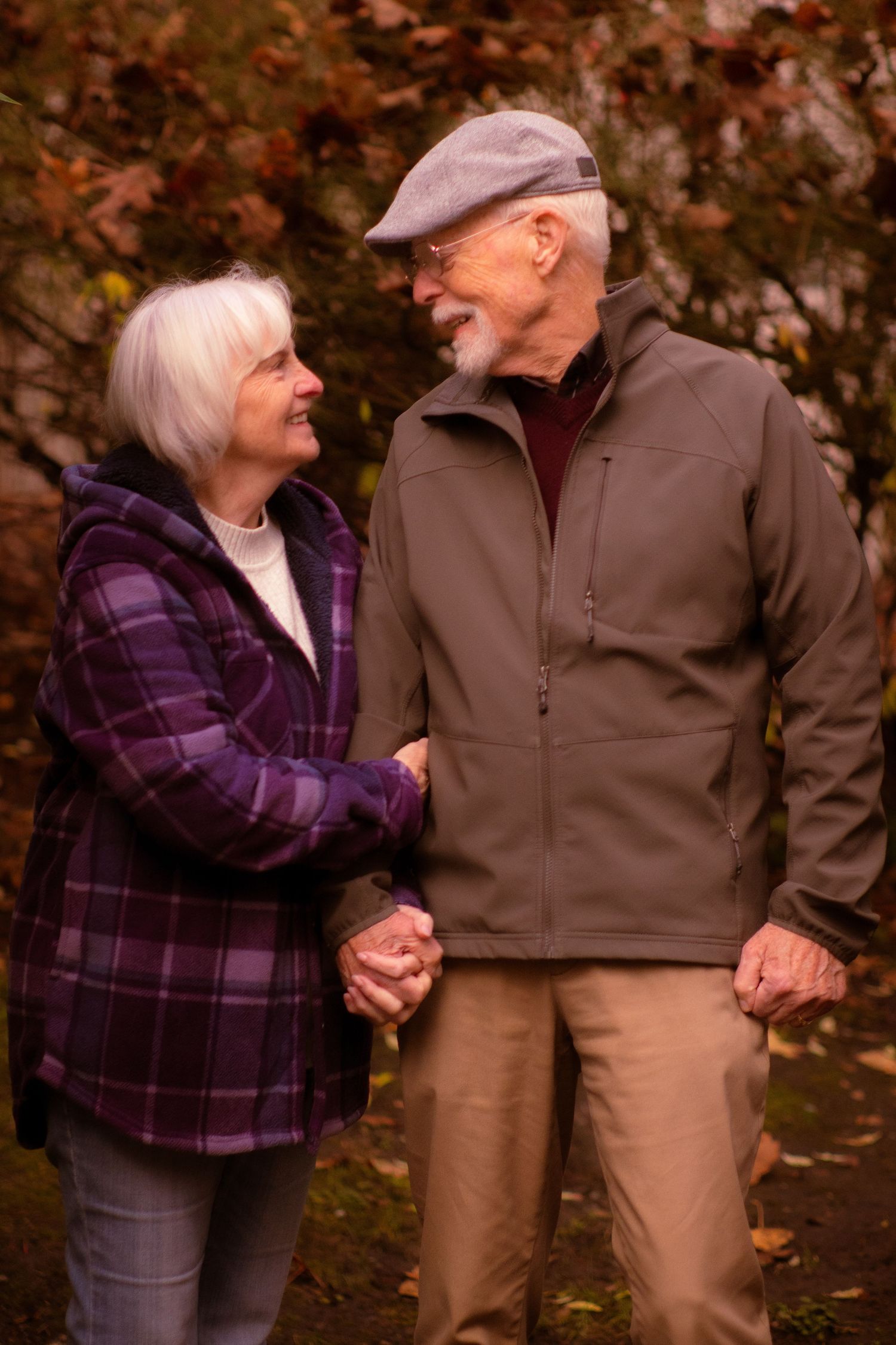 Smiling elderly couple holding hands and gazing at each other lovingly in an autumn park setting.