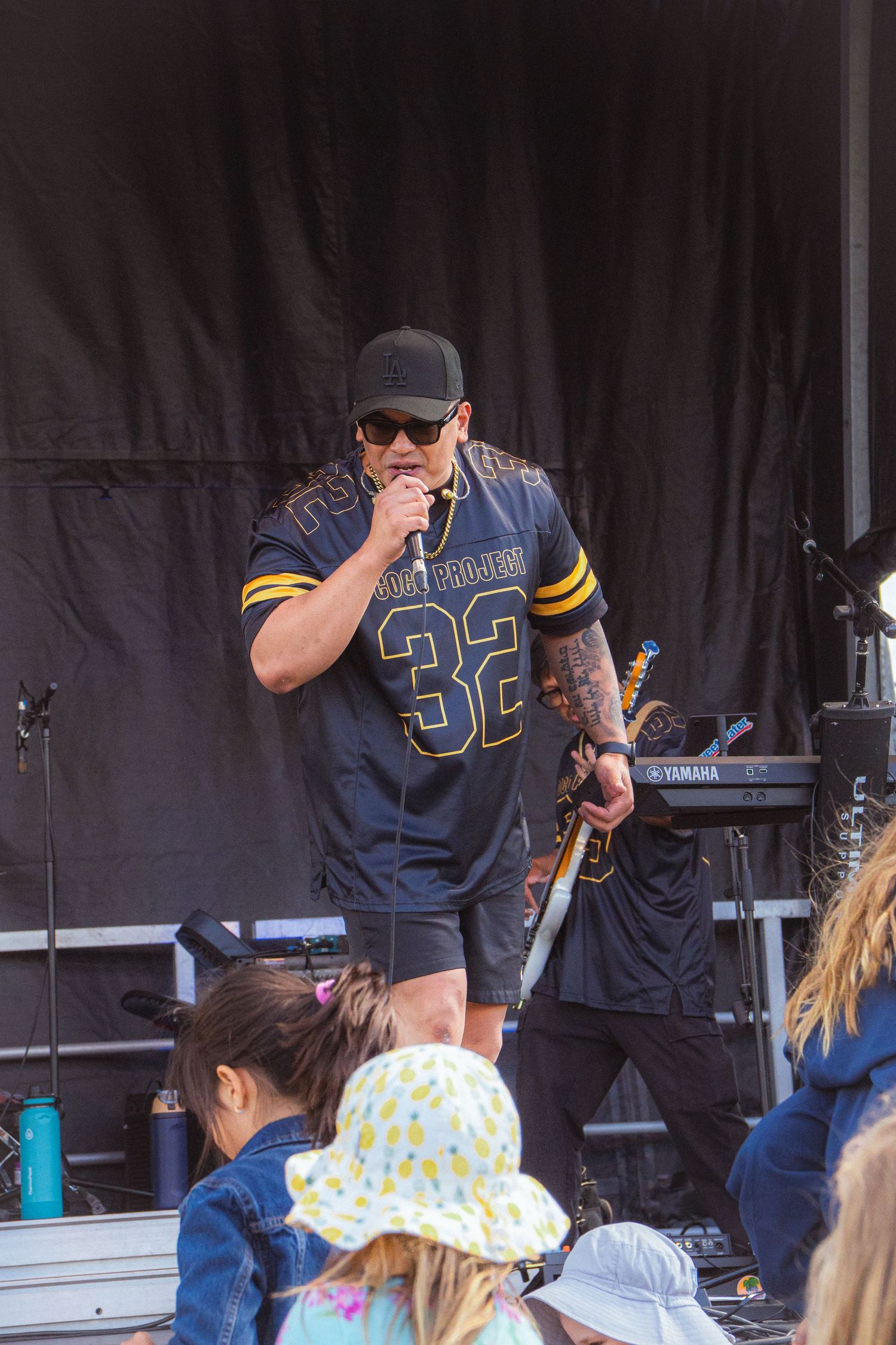 Tattooed male vocalist in #32 jersey sings into microphone on outdoor festival stage.