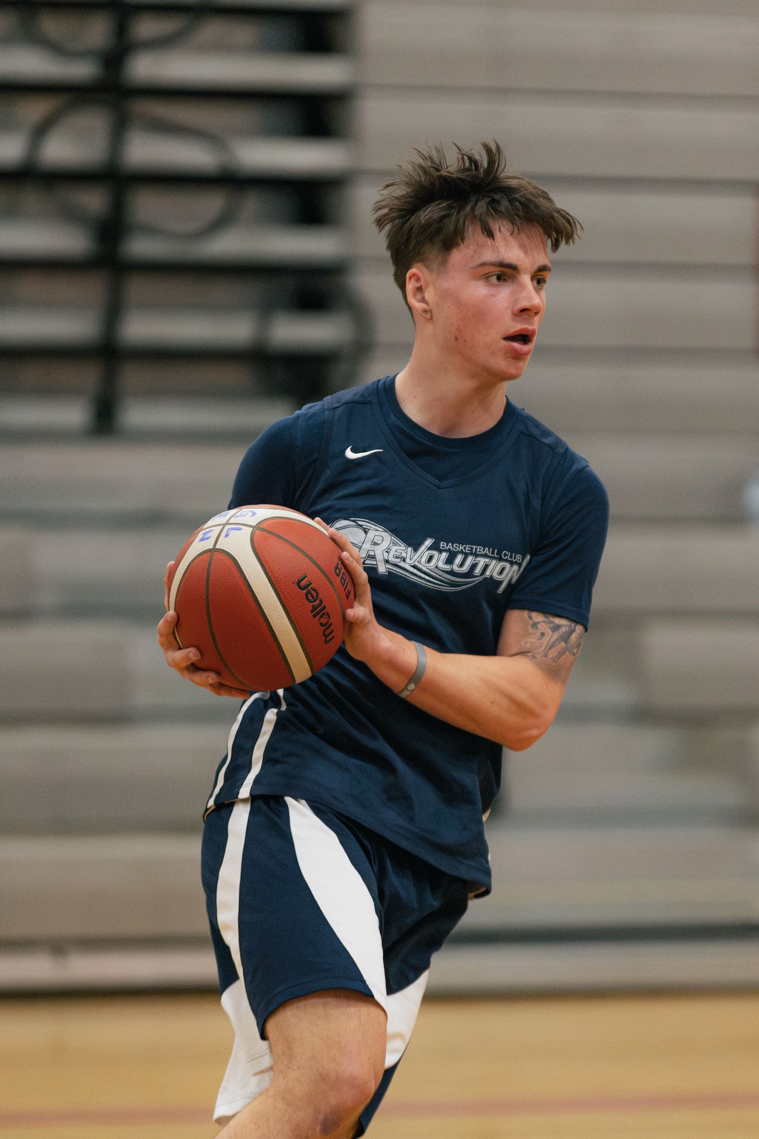 Young male basketball player in navy Revolution shirt holds ball ready to pass on indoor court.