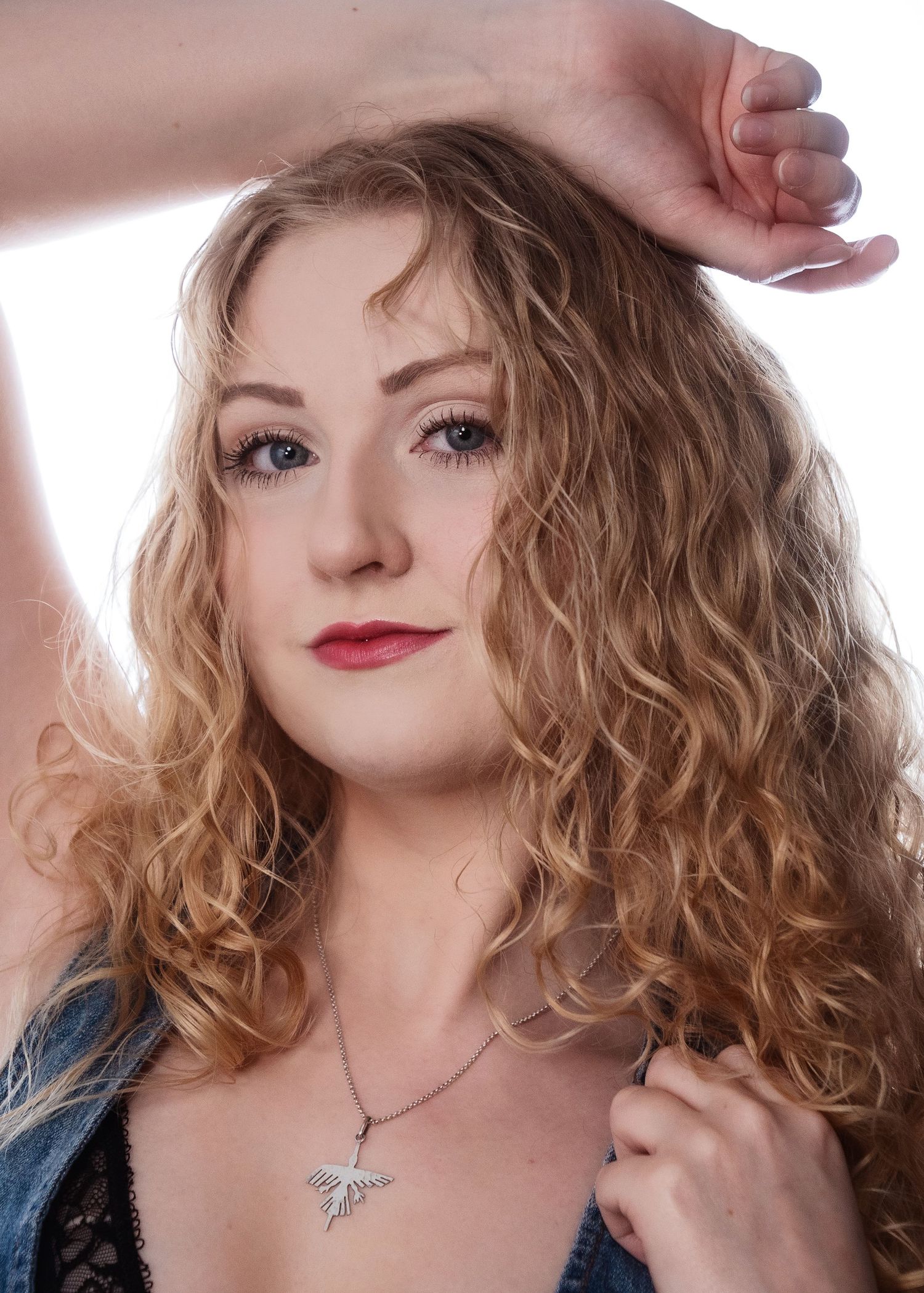 Young woman with curly blonde hair, red lips, and a silver necklace posing in a studio portrait.
