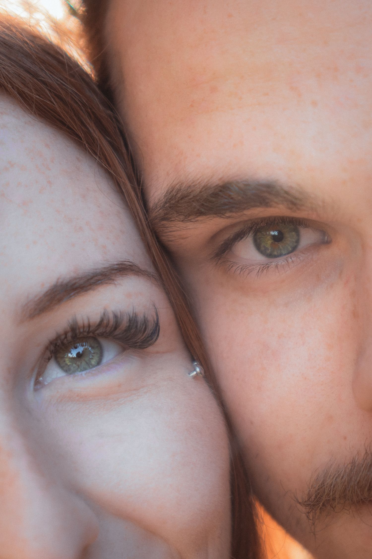 Close-up portrait of a couple with striking green eyes and freckles pressed cheek to cheek.