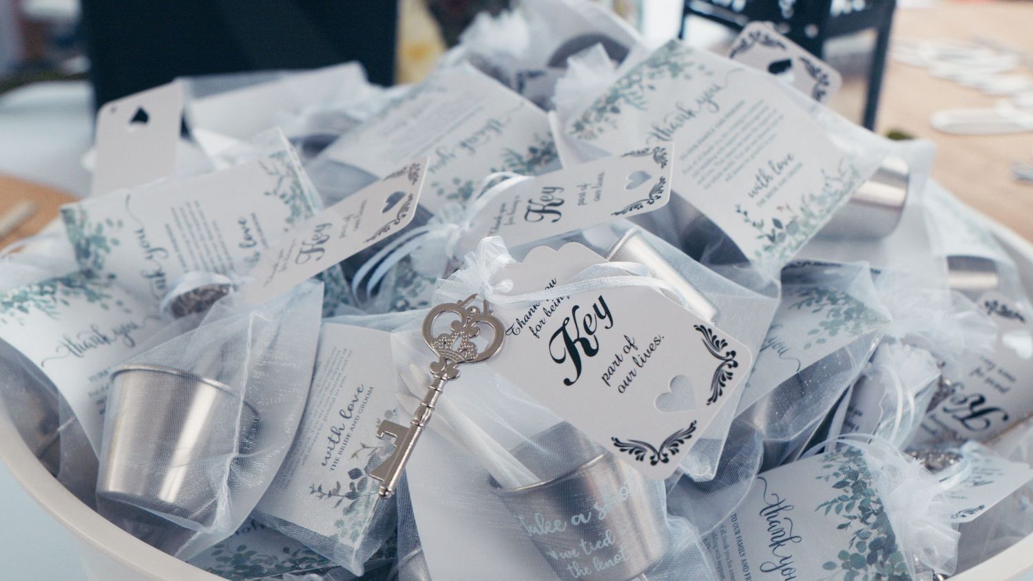 Elegant wedding favor bags with gold key charms and floral tags displayed in a decorative bowl.