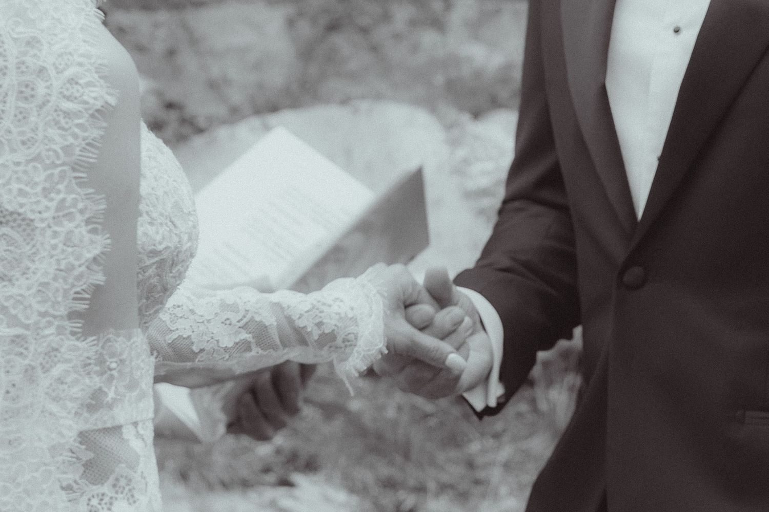 Black and white photo of bride and groom holding hands during outdoor wedding ceremony.