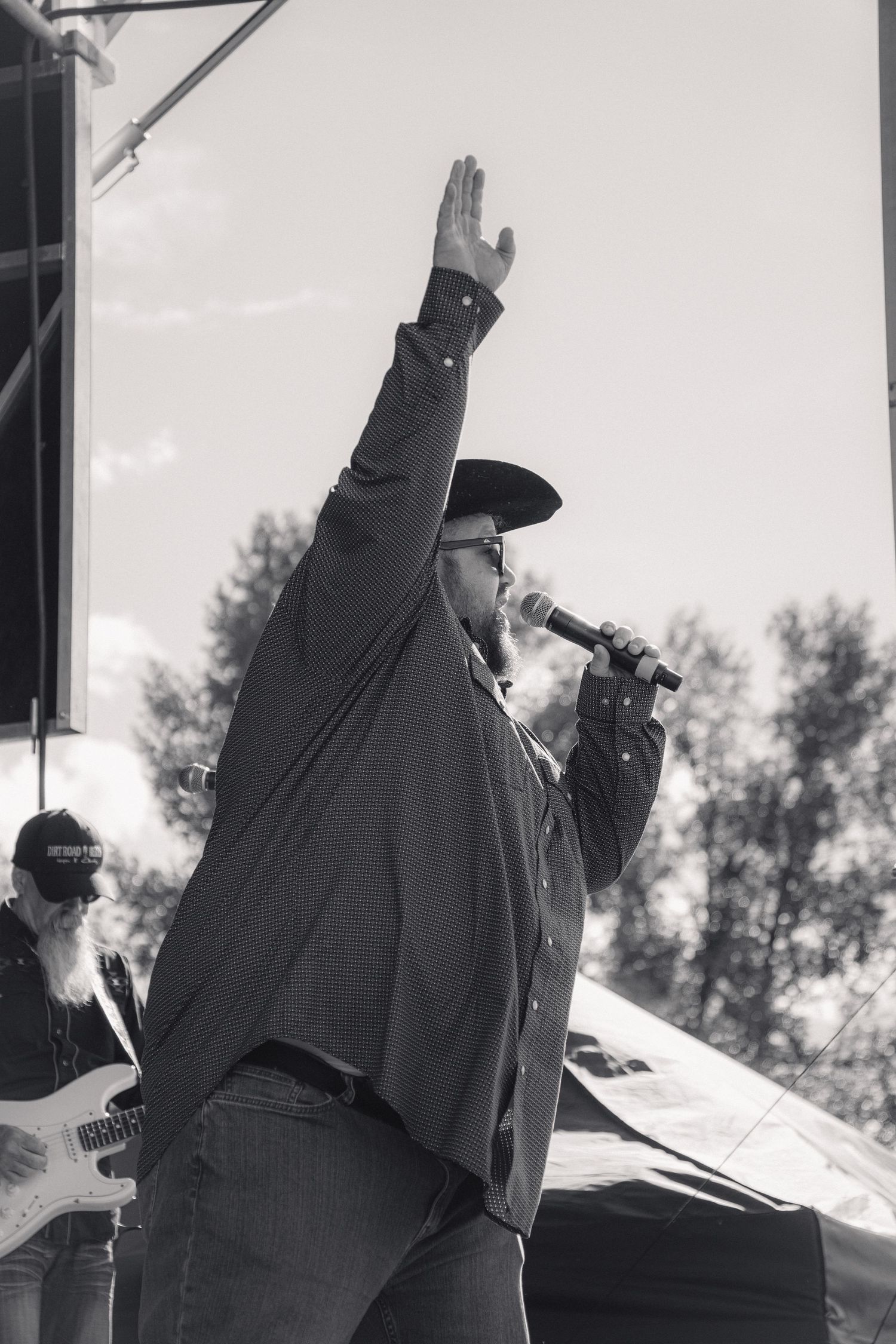 Black and white photo of country singer raising hand while performing on outdoor stage.