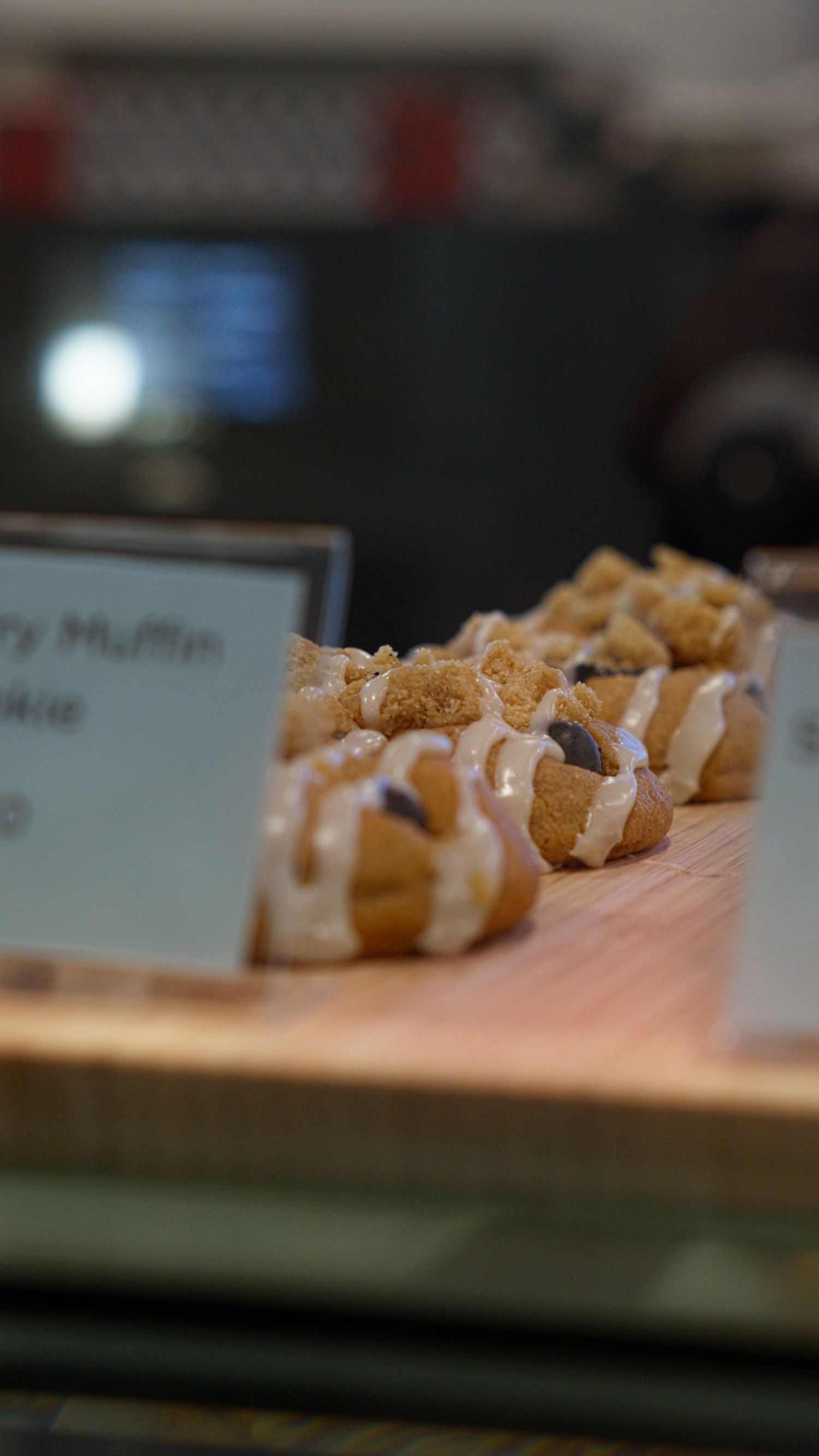 Close-up of glazed cream puff pastries with crumble topping displayed on wooden board in bakery case.