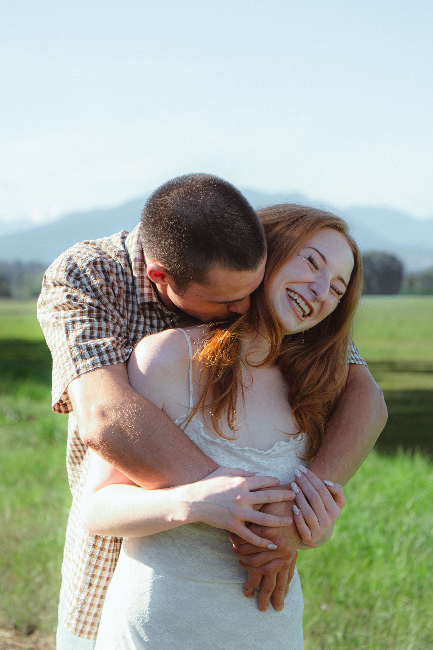 Happy couple embracing outdoors in a green field with mountains in the background on a sunny day.