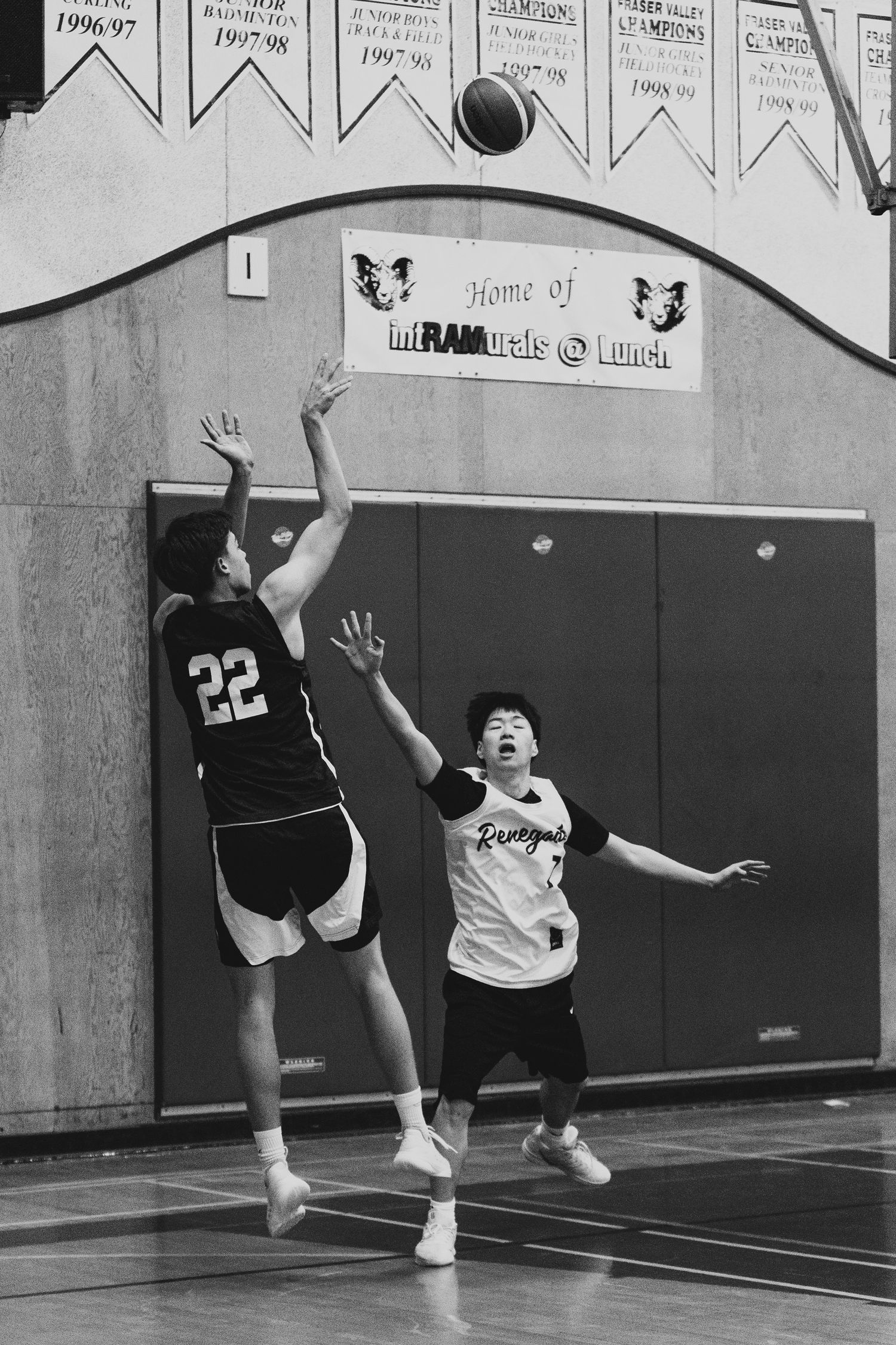Player #22 rises for a jump shot over a Renegades defender in indoor basketball game.