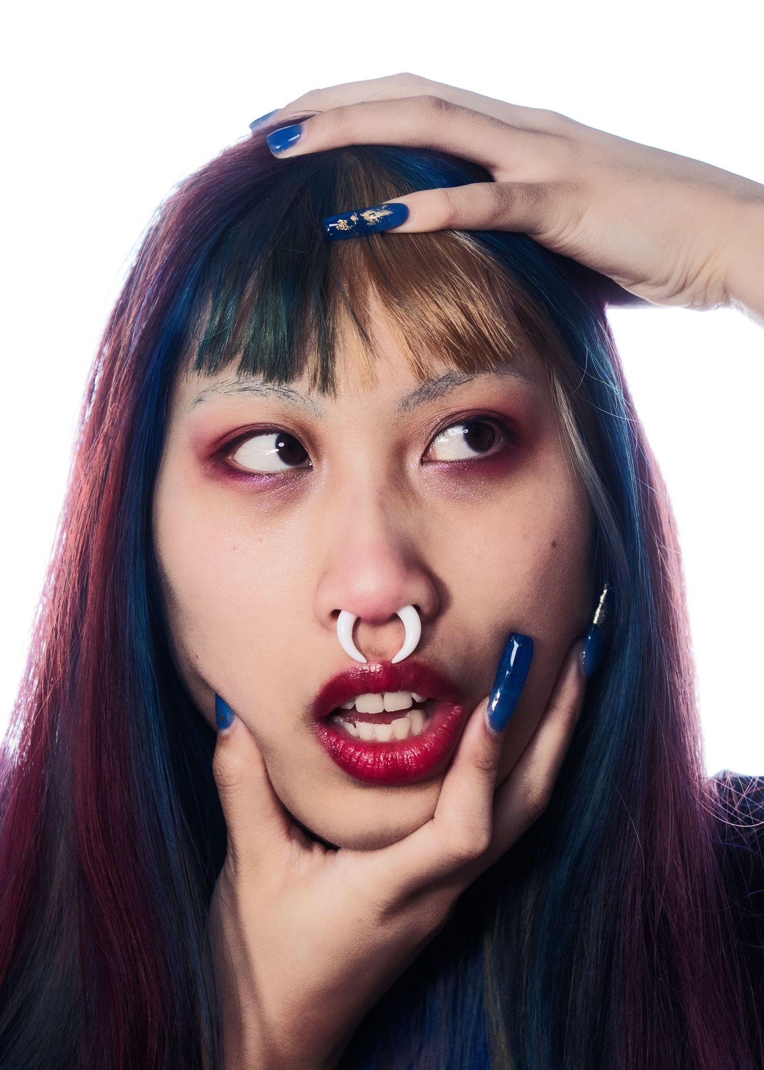 Young woman with multicolored hair, septum ring, dramatic red eye makeup, and long blue nails.