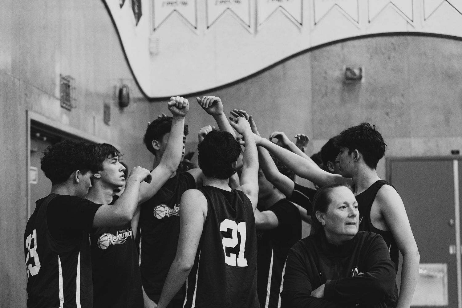 A youth basketball team huddles together with their coach in a black and white gym photo.