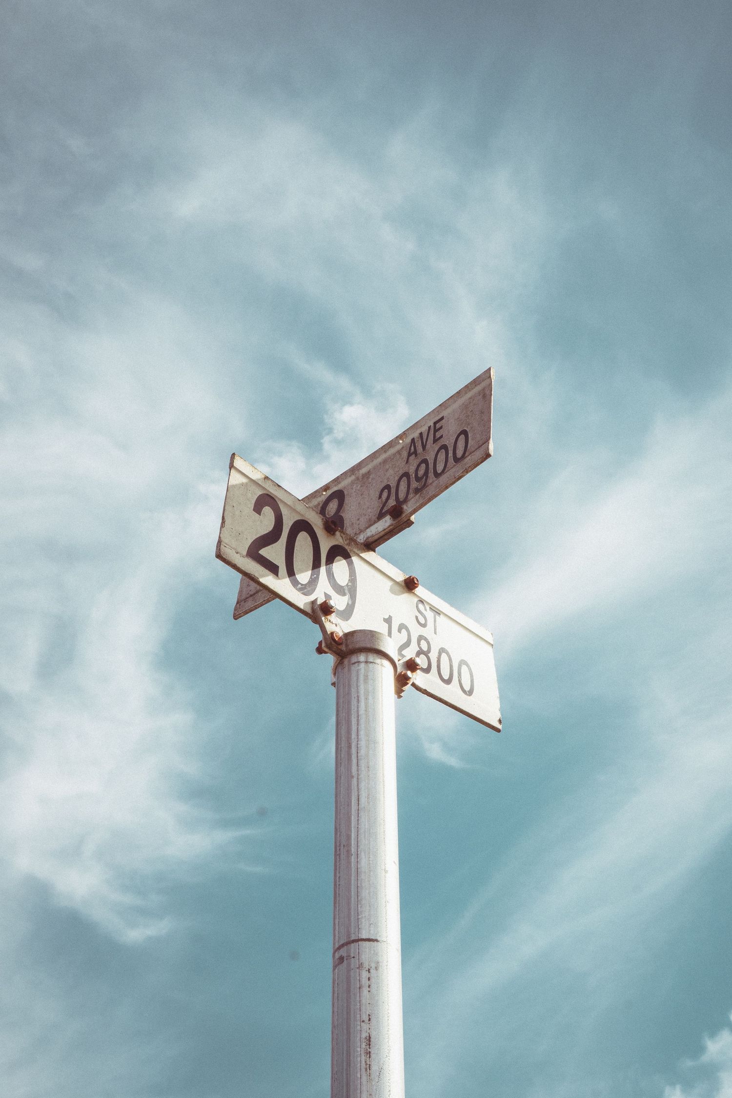Street sign post showing 209th Ave and Street intersections against blue cloudy sky.