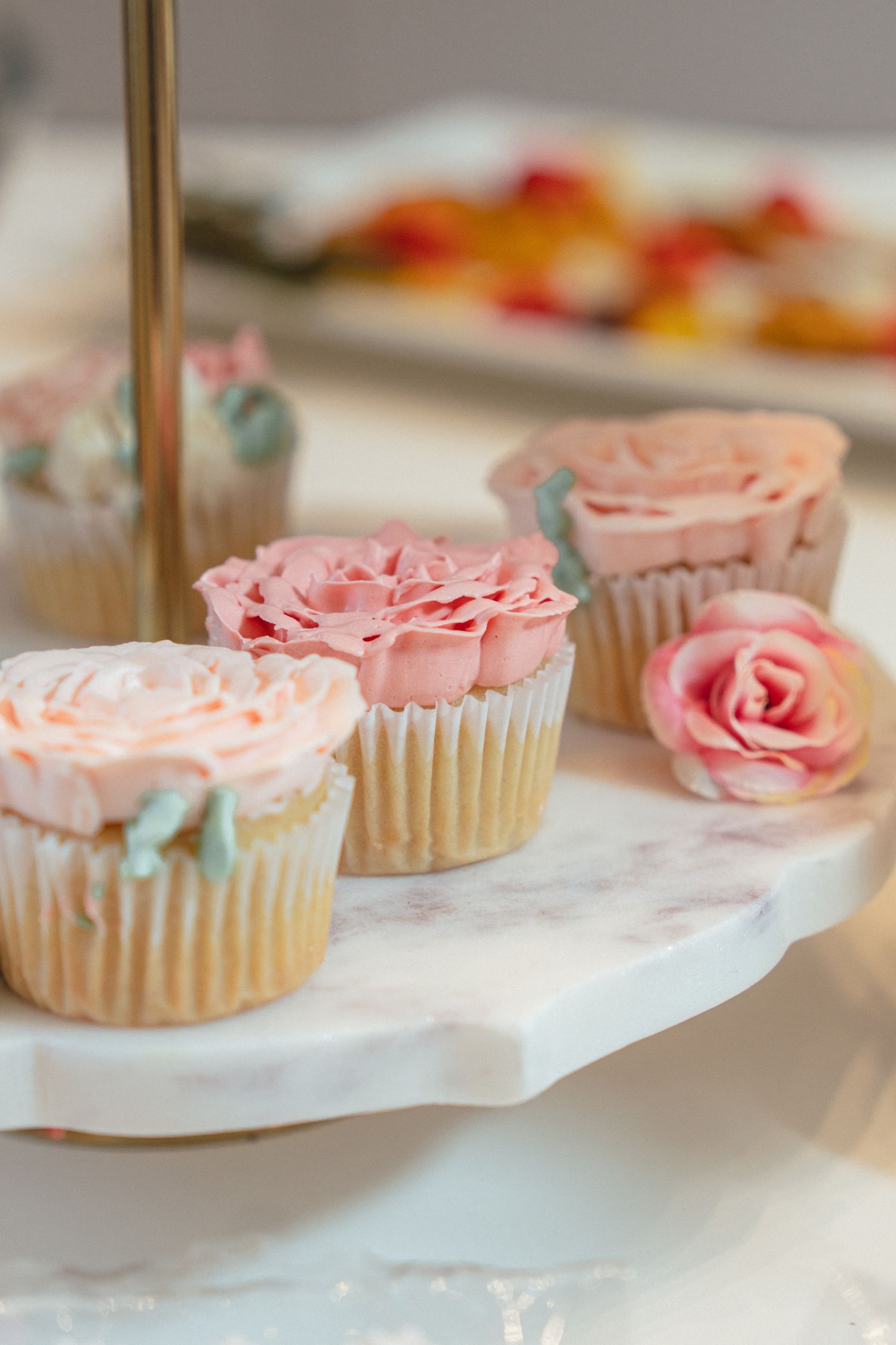 Elegant cupcakes with pink rose frosting on a marble tiered stand, perfect for weddings or special occasions.