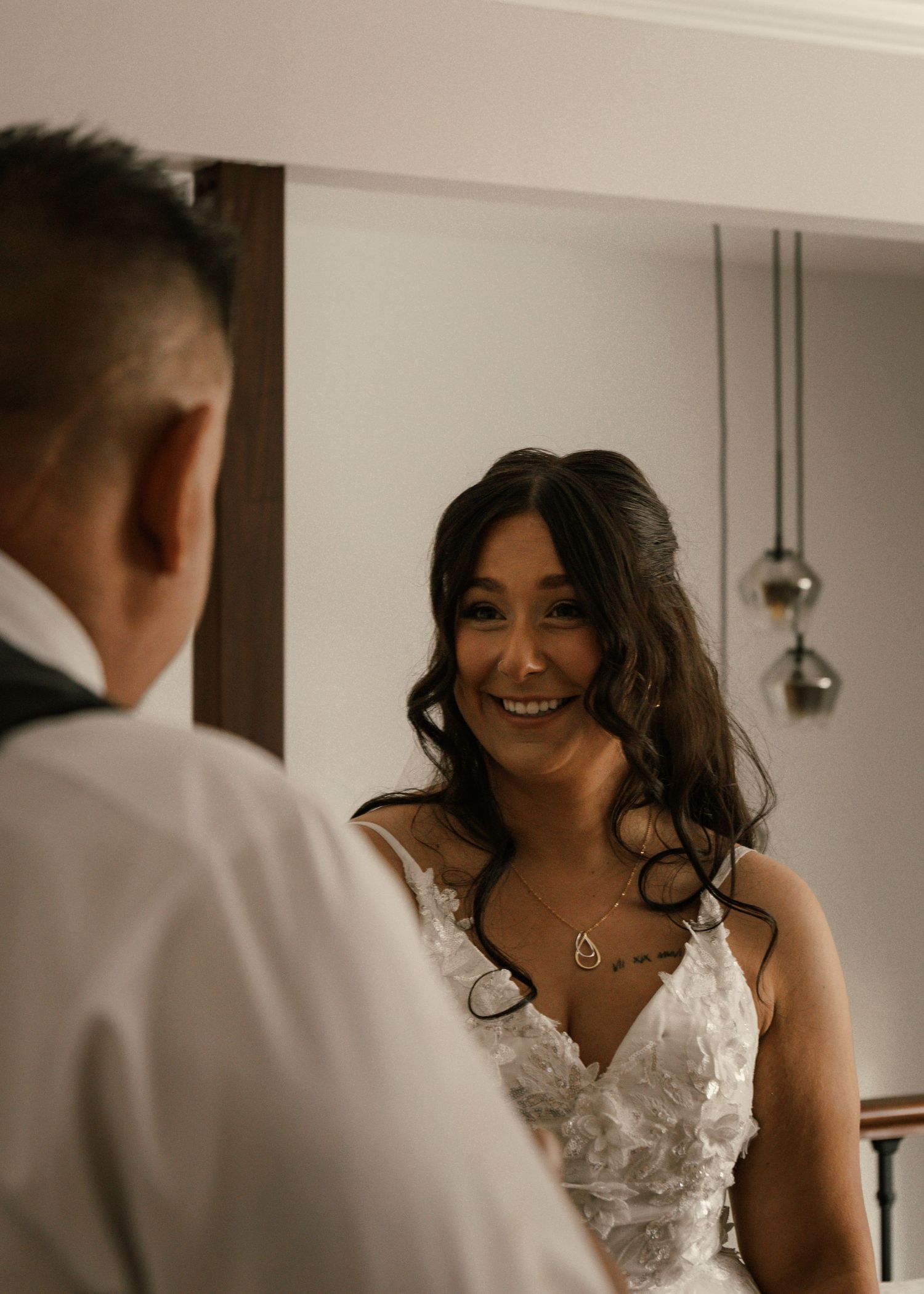 Bride in white lace gown smiling at groom during first look moment indoors.