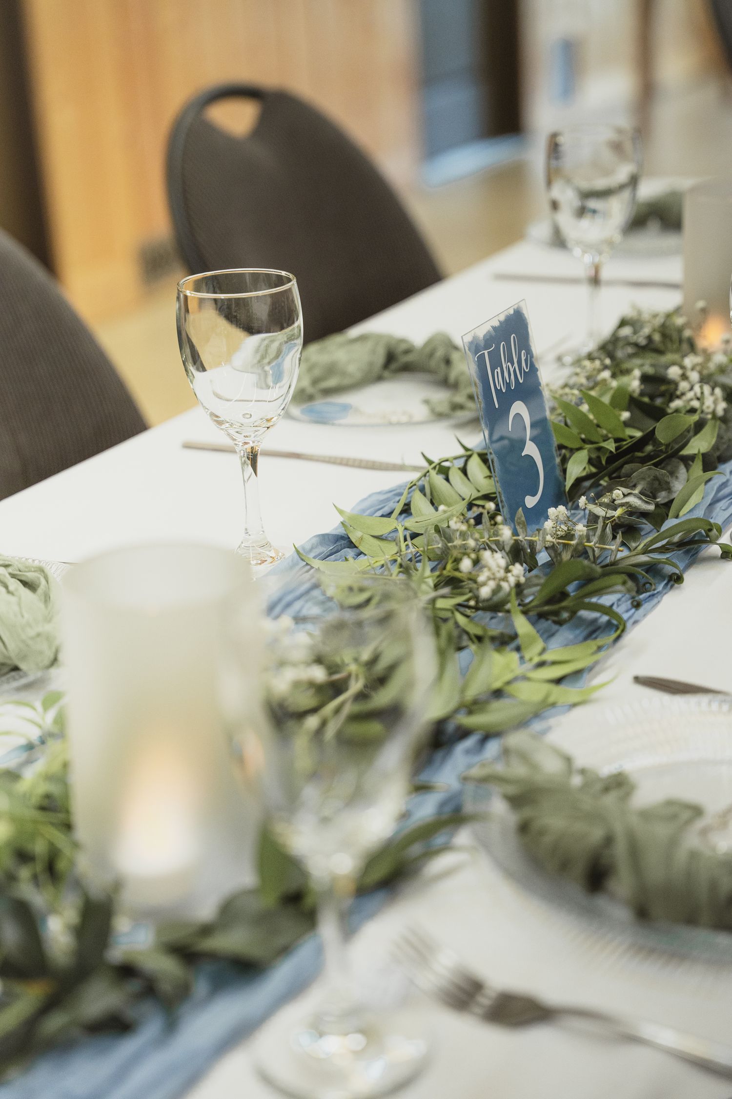 Elegant wedding table setting with greenery runner, candles, and Table 3 card.