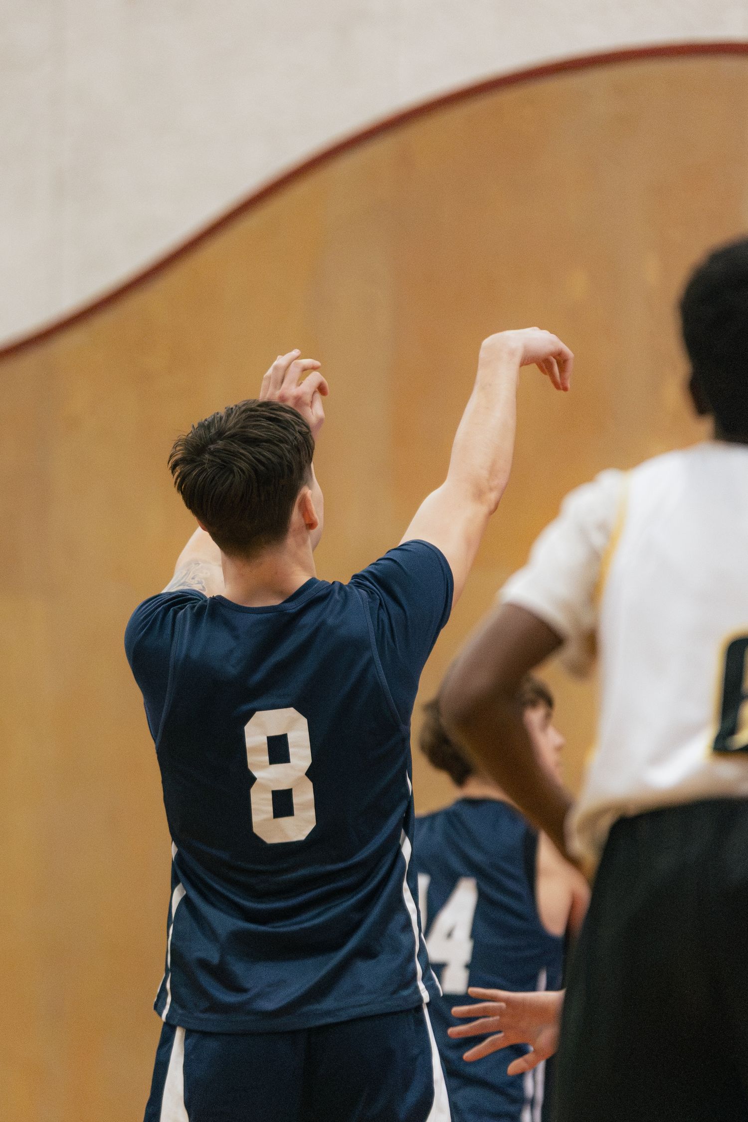 Basketball player wearing navy jersey #8 follows through on a shot with arm raised during indoor team game.