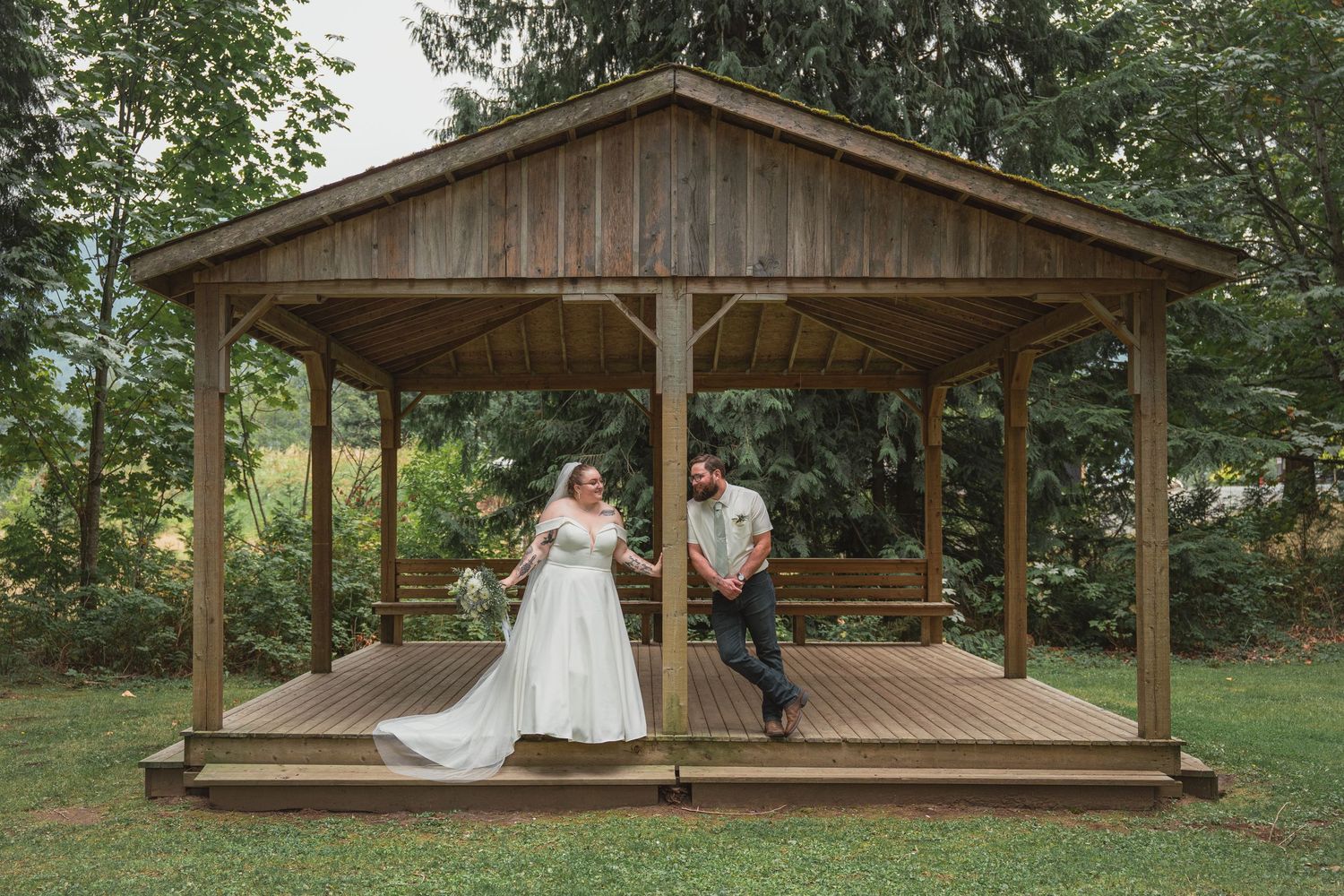 Bride and groom standing under a rustic wooden gazebo on a lush green lawn during outdoor wedding ceremony.