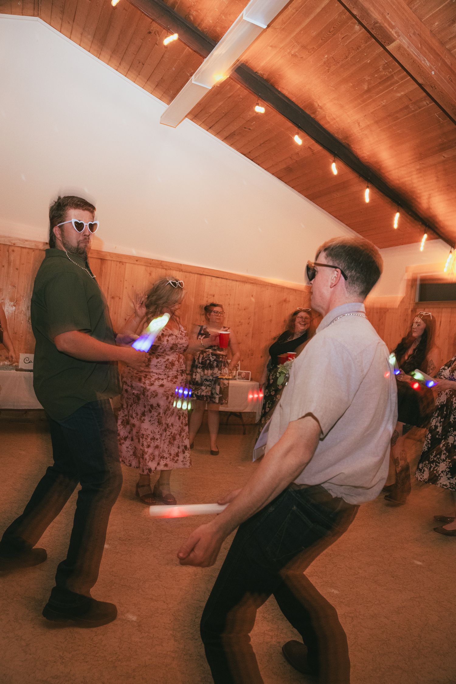 Two men dancing energetically with glow sticks at wedding reception party.
