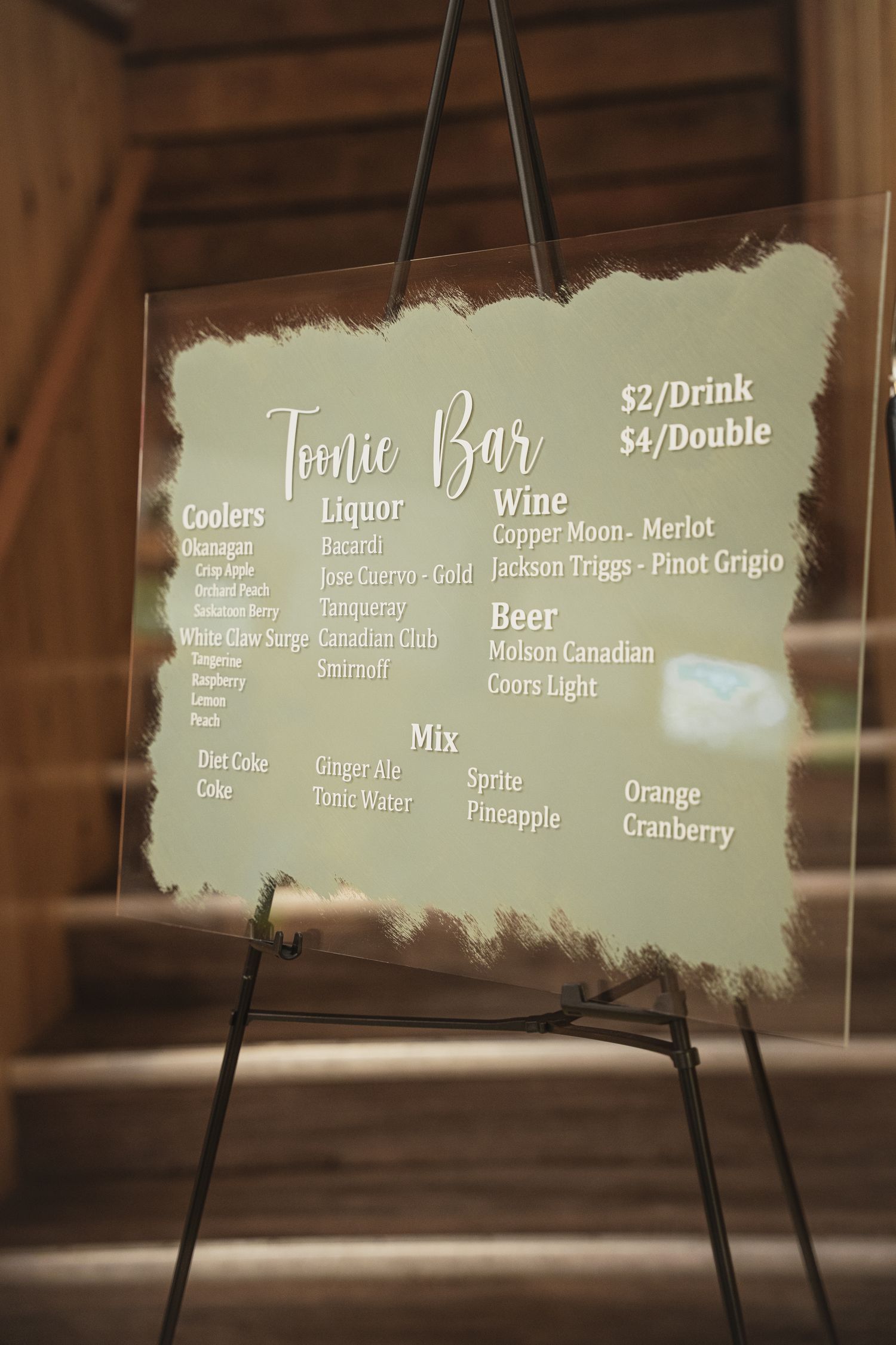 Elegant acrylic tonic bar menu sign on easel listing coolers, liquor, wine, beer and mix options at wedding reception.