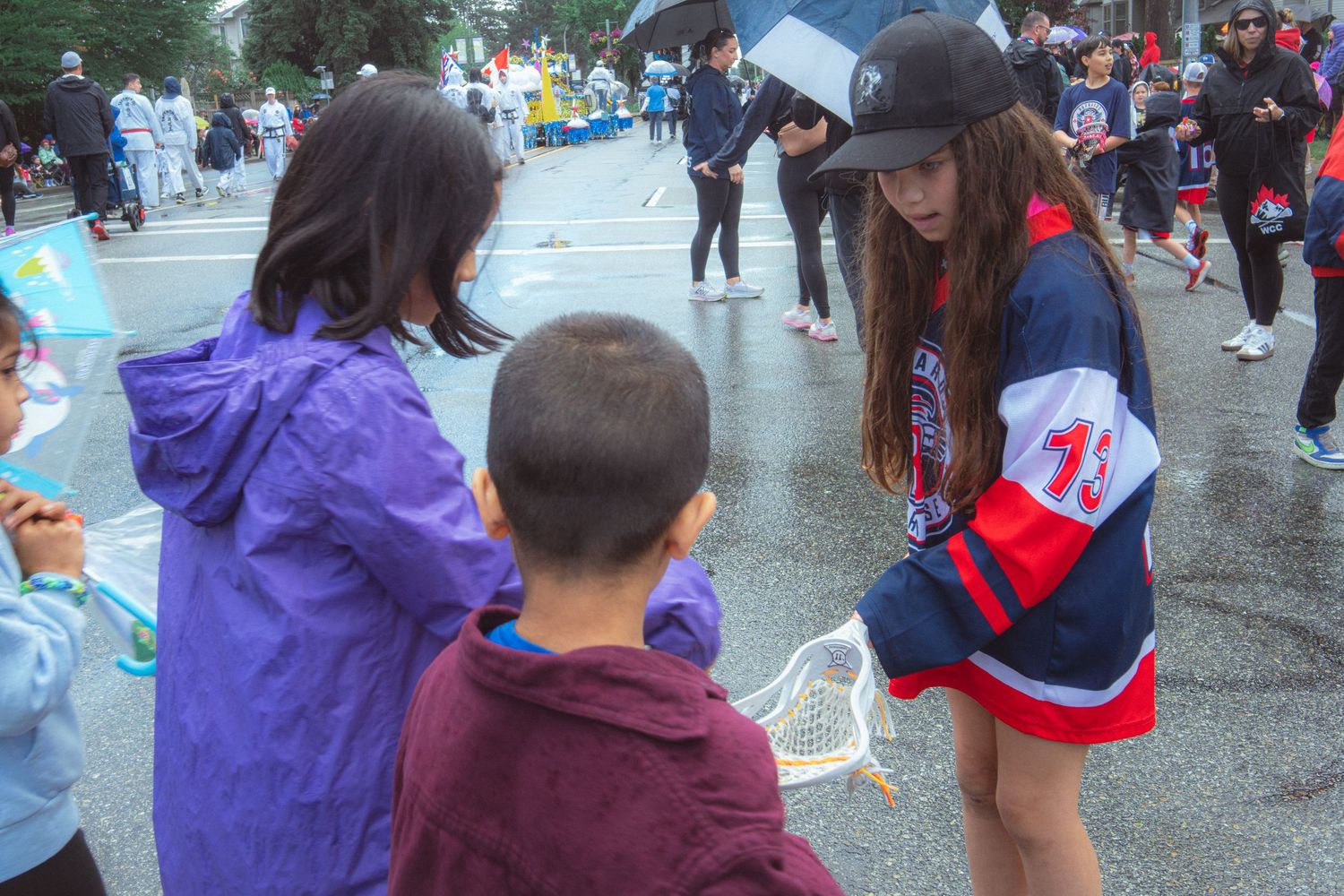 Young girl in hockey jersey interacting with children during rainy street parade event.